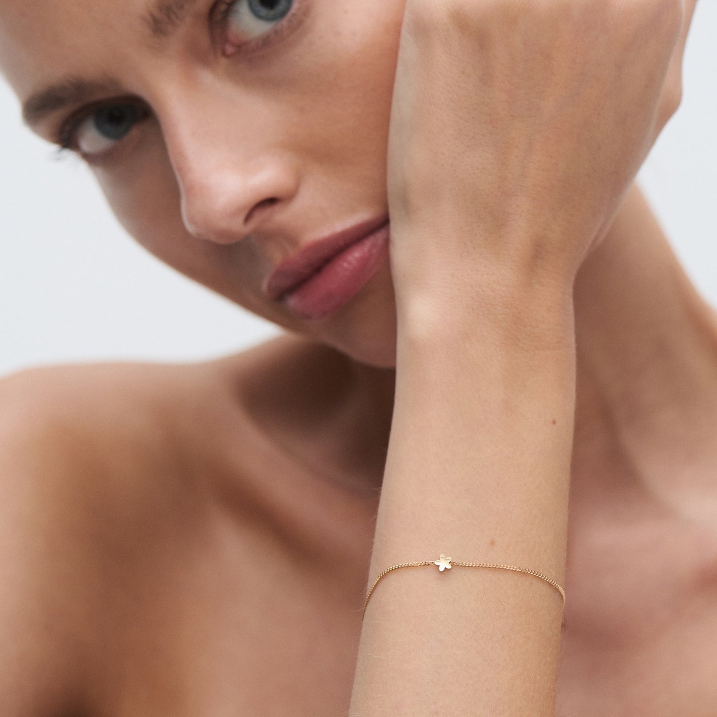 Woman showcases a delicate gold bracelet with a small star charm. Luxurious jewellery, elegant design, close-up on wrist and face.