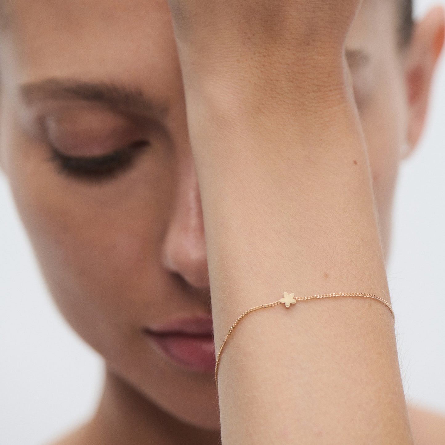 Close-up of a woman wearing a delicate gold bracelet with a small star charm. She's posing with her hand over her forehead, exuding elegance.