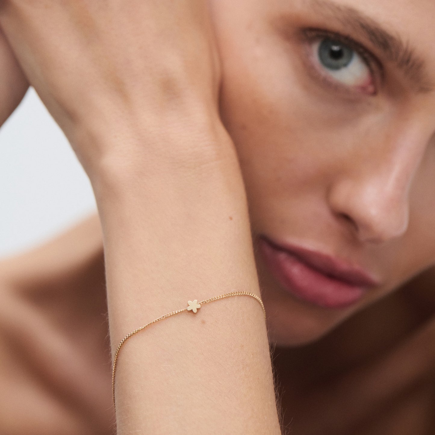 Close-up of a woman's wrist adorned with a delicate gold bracelet featuring a small flower charm, highlighting luxury jewellery.