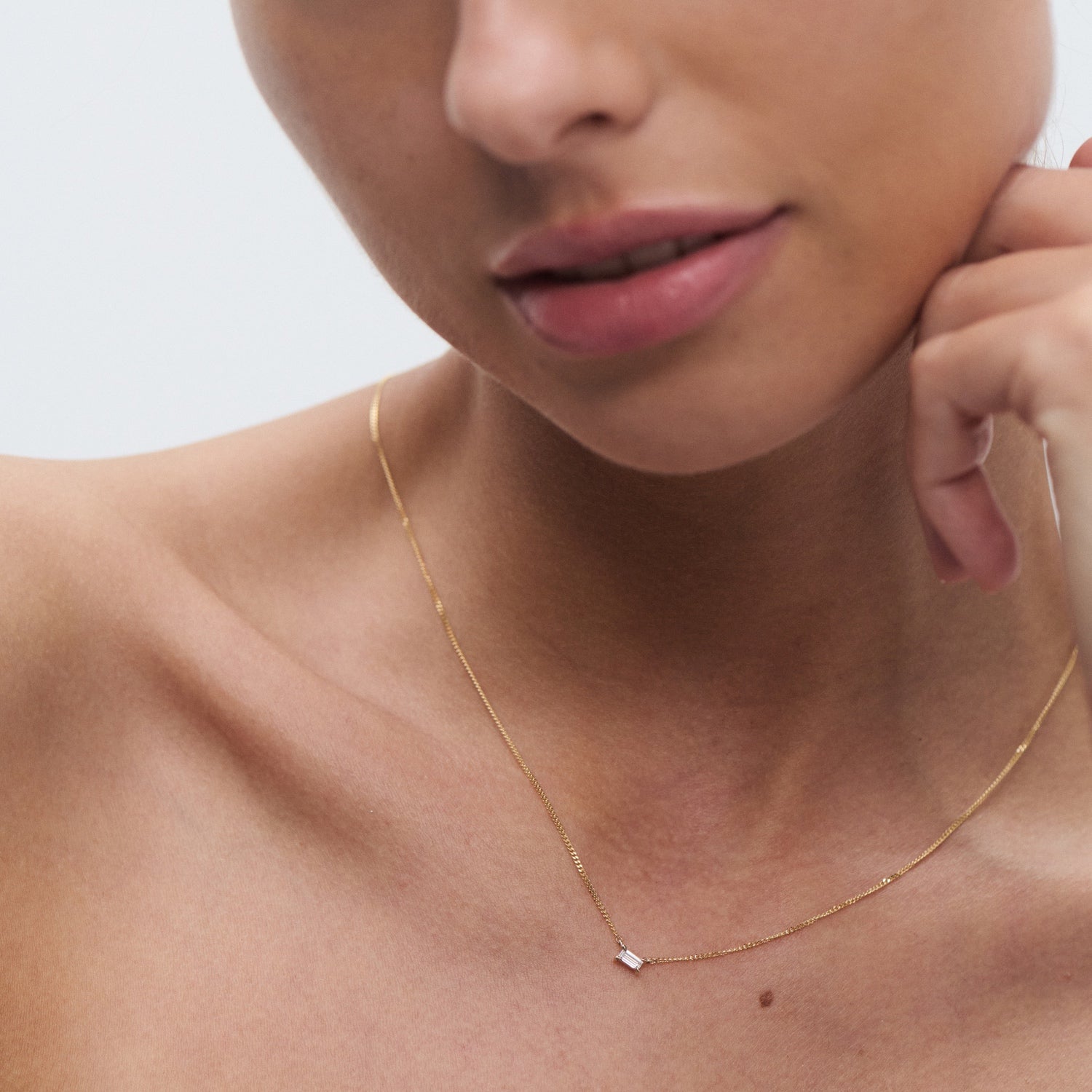 Woman wearing a minimalist gold necklace with a small diamond pendant, showcasing elegance and luxury jewellery details.