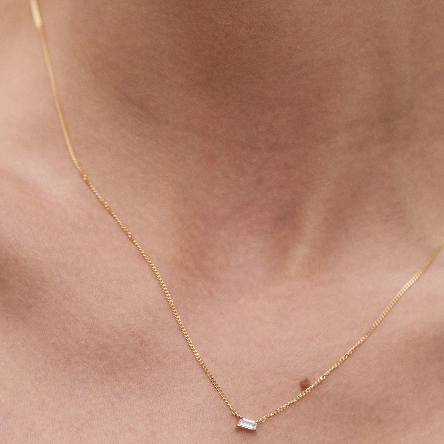 Elegant gold necklace with a single rectangular diamond pendant on a person's neck, showcasing minimalist luxury jewellery.