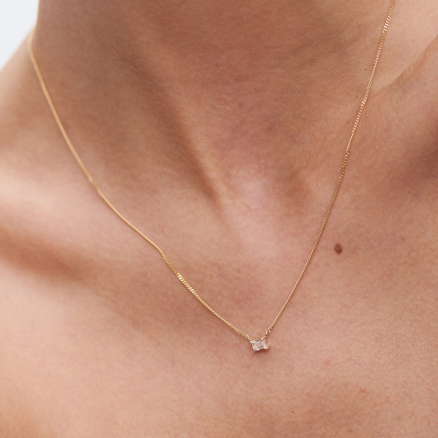 Elegant gold necklace with a small, square pendant on a woman's neck, highlighting minimalist luxury jewellery style.