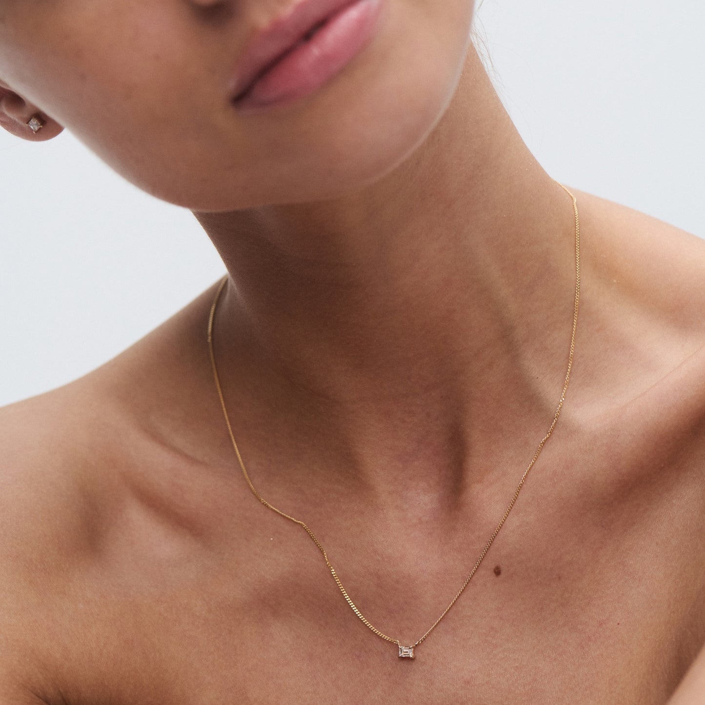 Close-up of a gold necklace with a small square pendant on a woman’s neck, highlighting luxury jewellery's elegance and simplicity.
