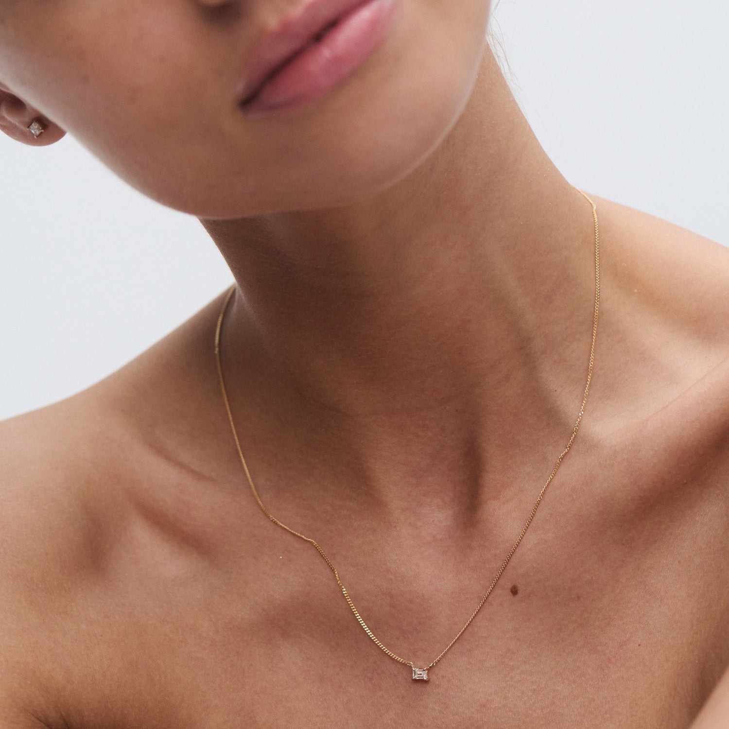 Close-up of a gold necklace with a small square pendant on a woman’s neck, highlighting luxury jewellery's elegance and simplicity.