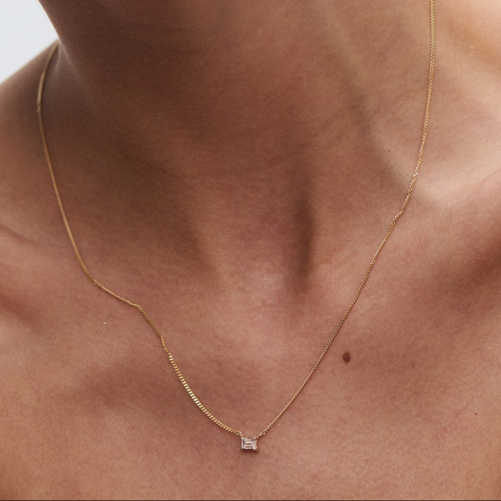 Close-up of a gold necklace with a small square pendant on a woman’s neck, highlighting luxury jewellery's elegance and simplicity.