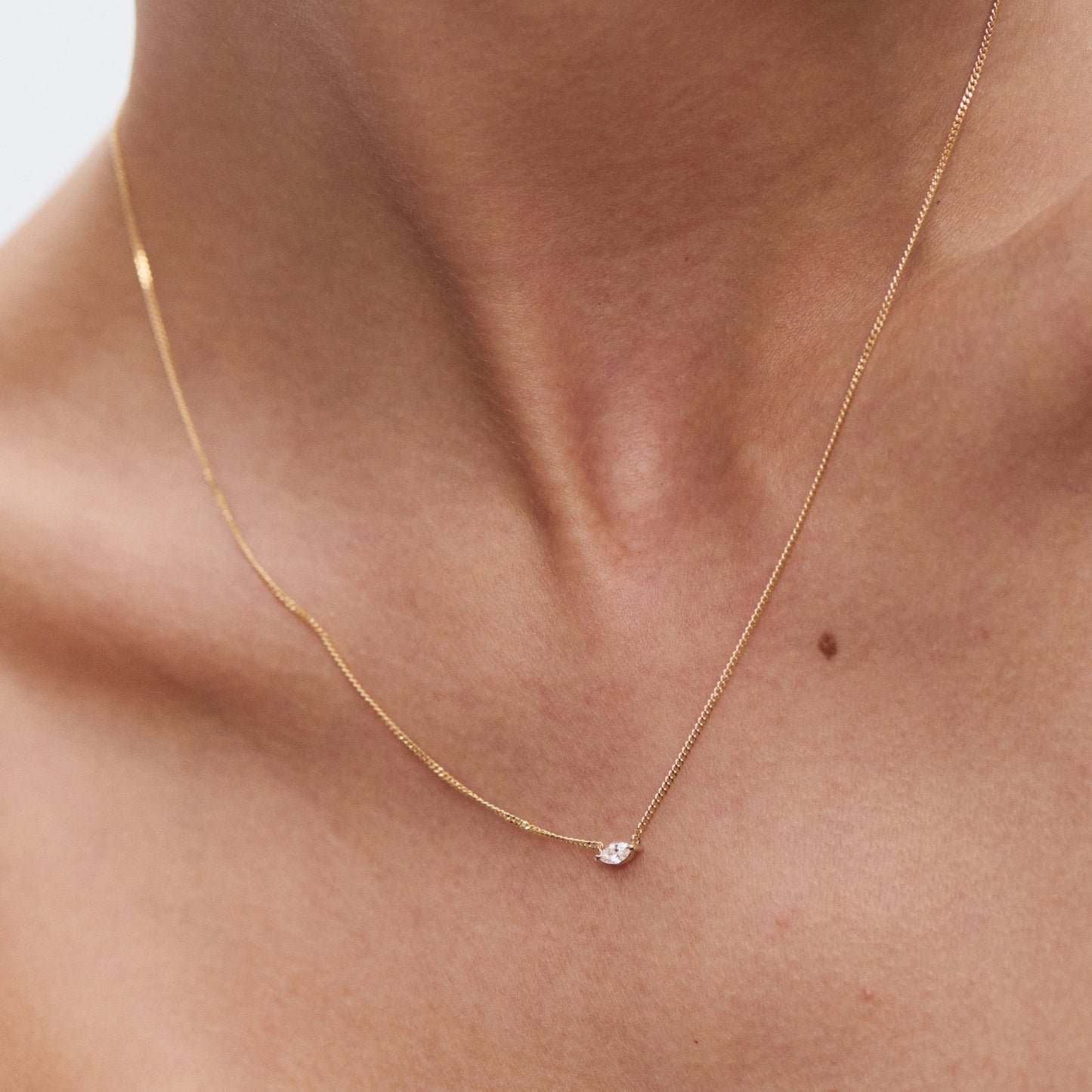 Elegant gold necklace with a single diamond pendant worn on a model's neck; luxury jewellery detail.