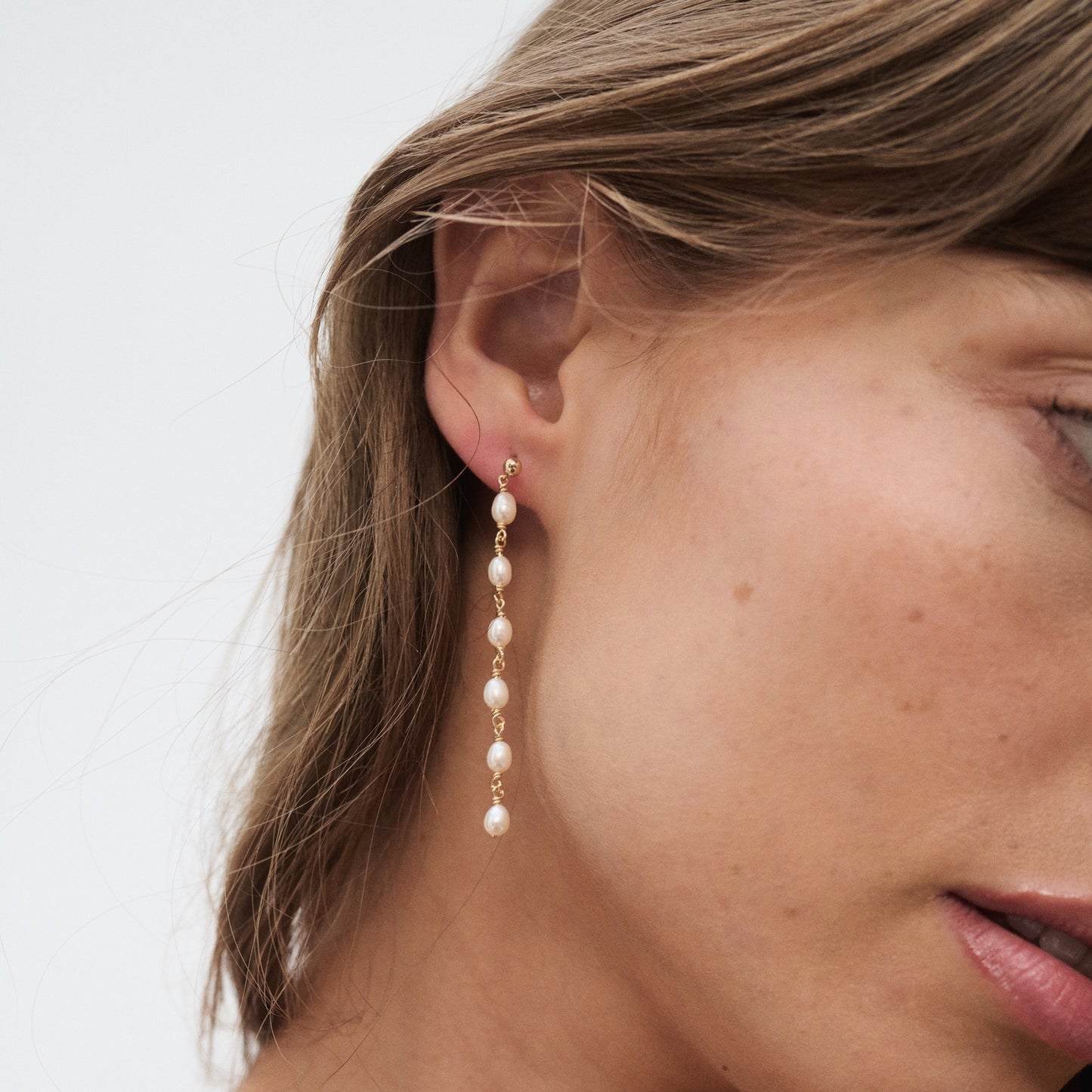Close-up of a woman's ear wearing a luxury gold earring with cascading pearls, showcasing elegant jewellery design in natural light.