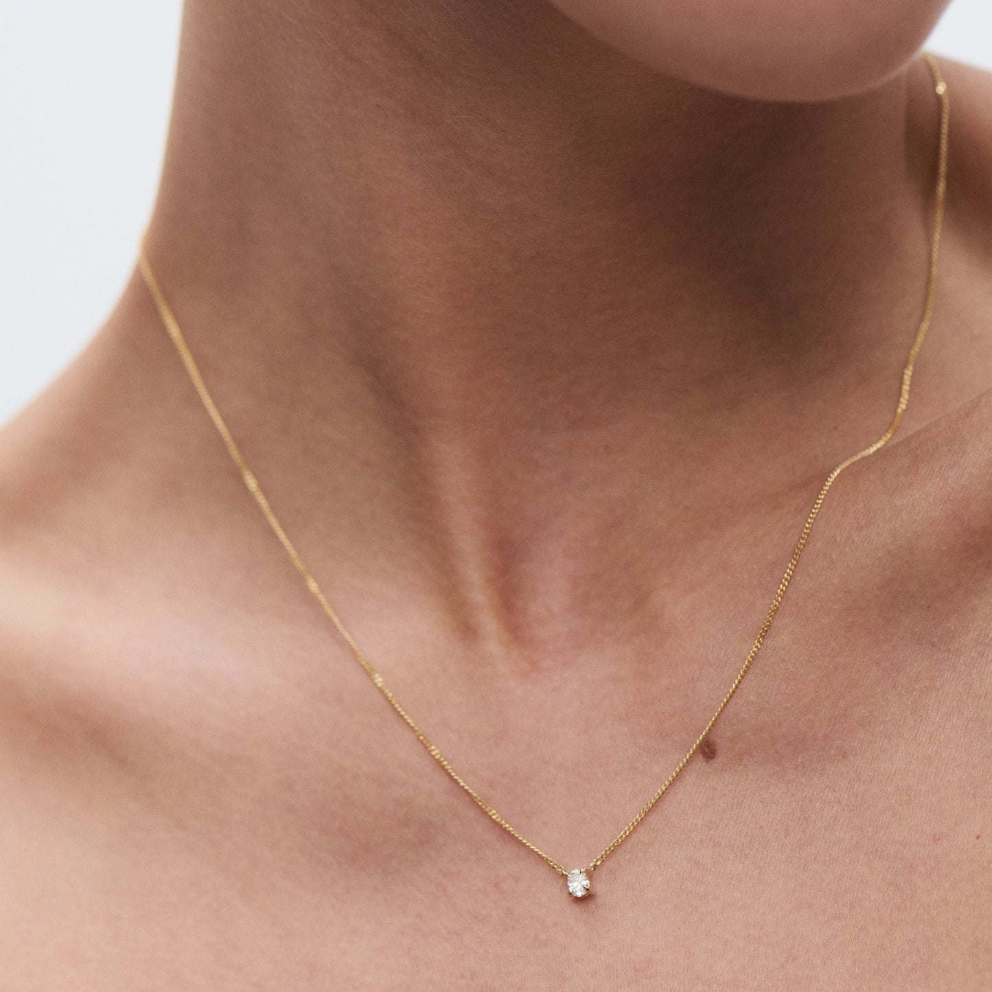 Elegant gold necklace with a single diamond pendant on bare skin, showcasing luxury jewellery design.