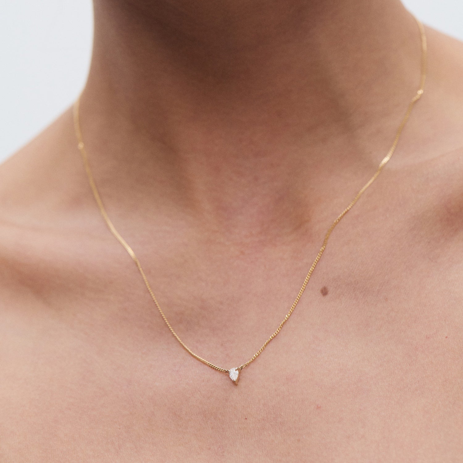 Delicate gold necklace with a small diamond pendant, elegantly worn on a person's neck against a plain background.