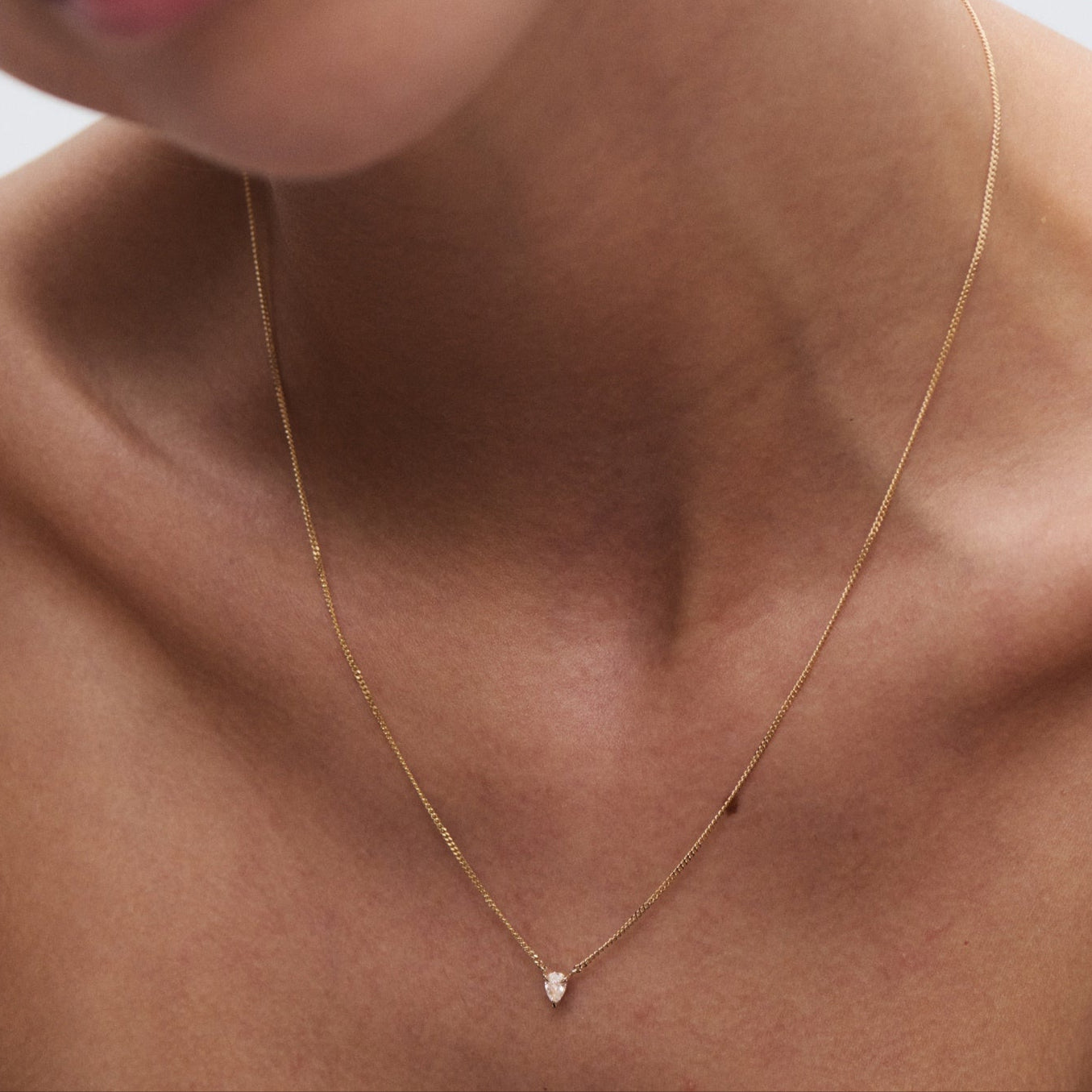 Close-up of a woman wearing a delicate gold necklace with a small teardrop pendant, showcasing luxury jewellery craftsmanship. [text overlay: Pear]