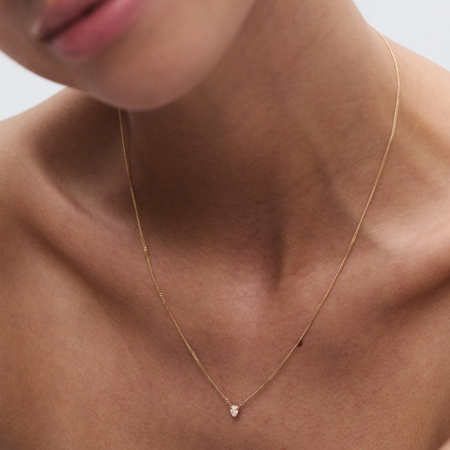 Close-up of a woman wearing a delicate gold necklace with a small teardrop pendant, showcasing luxury jewellery craftsmanship.