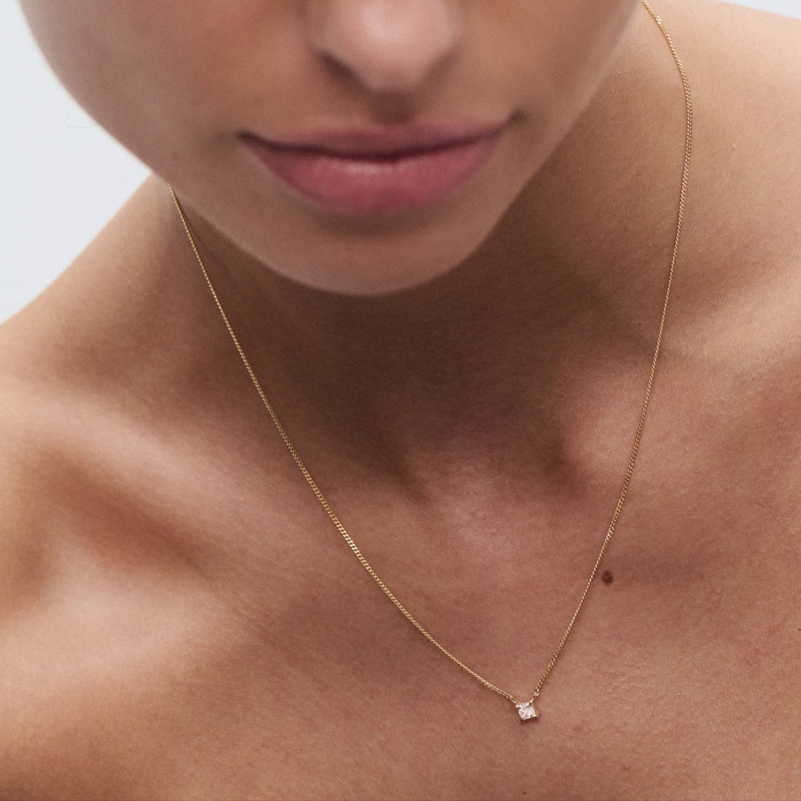 Woman wearing a delicate gold necklace with a small diamond pendant, showcasing luxury jewellery against soft-focus background.