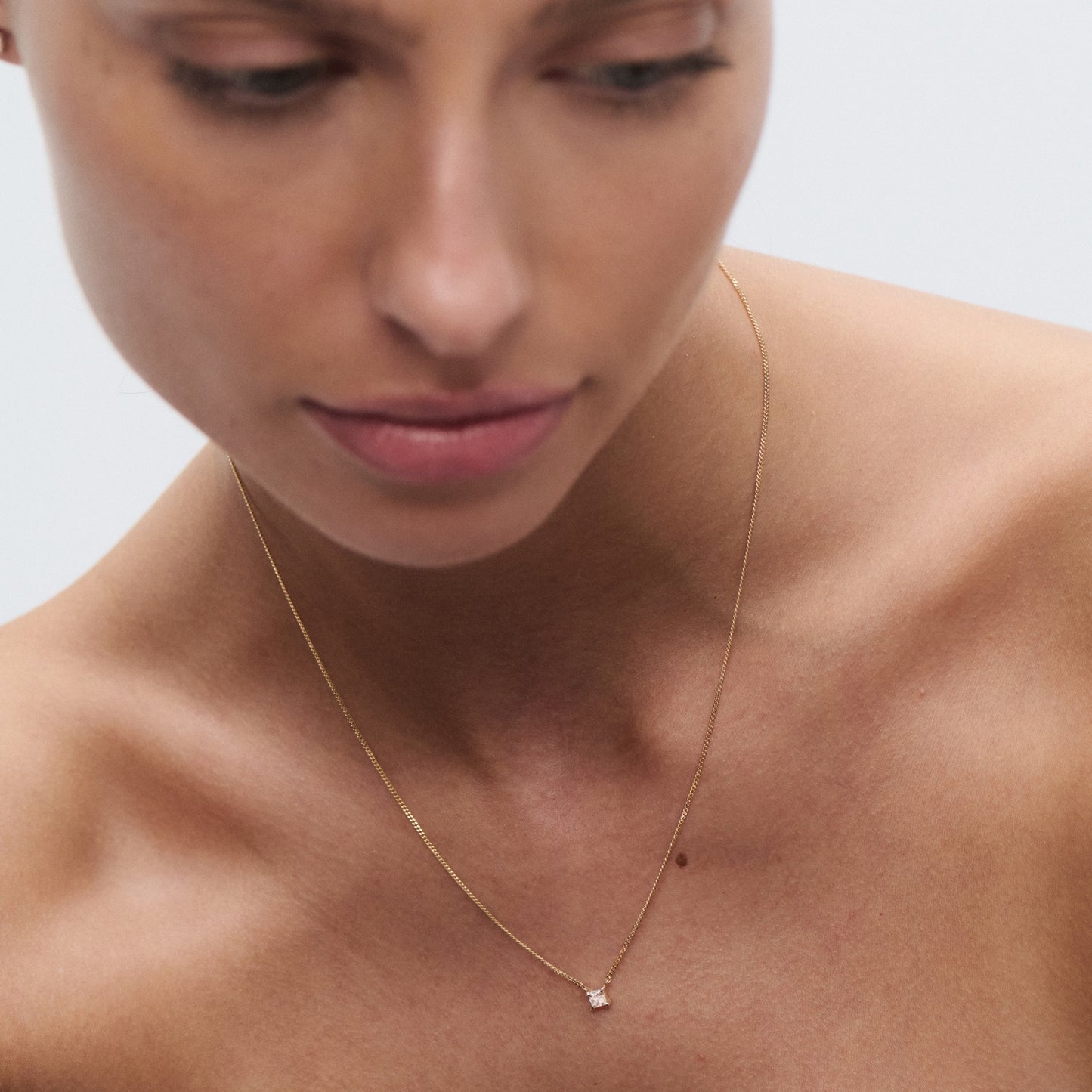 Woman wearing a delicate gold necklace with a small diamond pendant, showcasing luxury jewellery against soft-focus background.