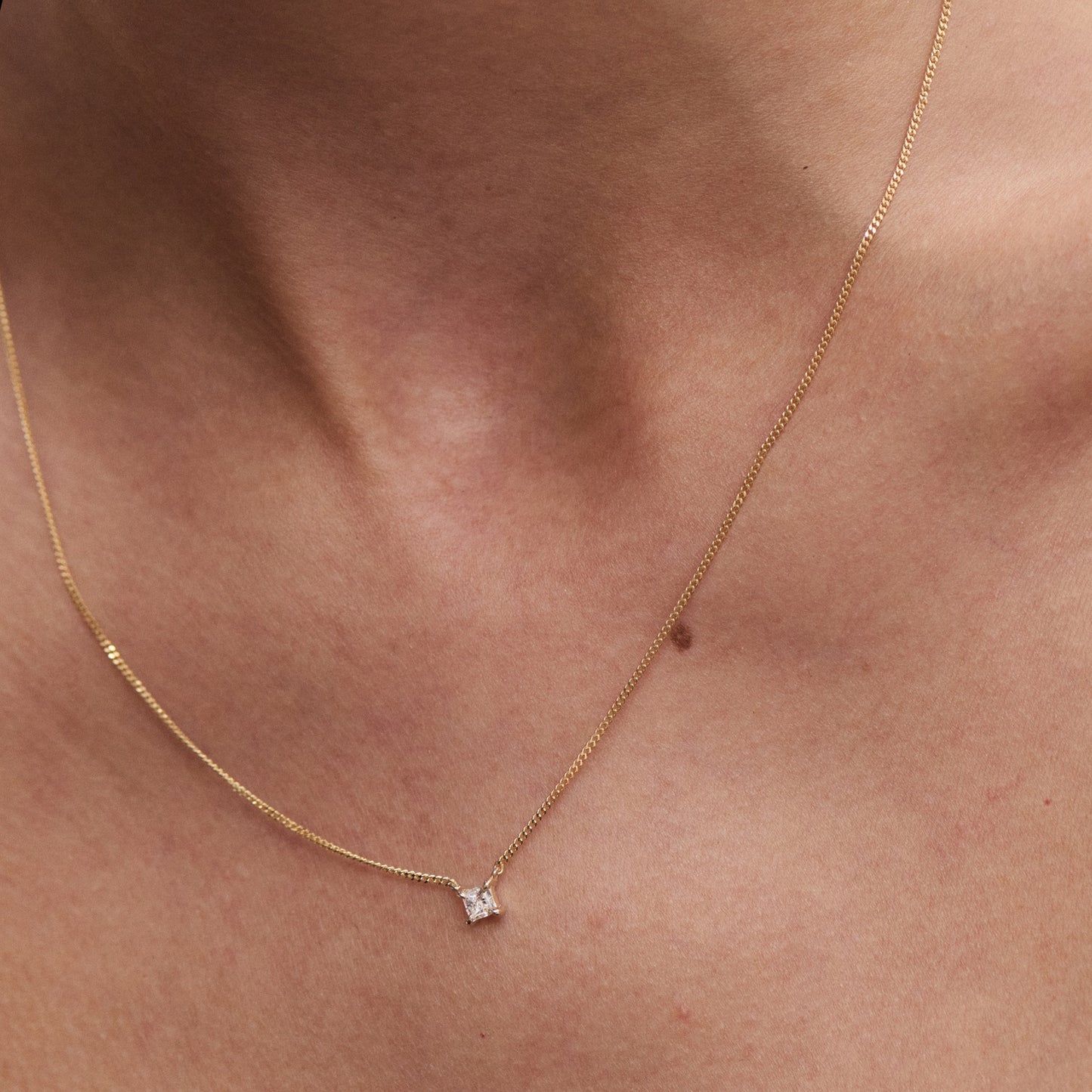 Delicate gold necklace with a small square diamond pendant on bare skin. Elegant and minimalist jewellery.