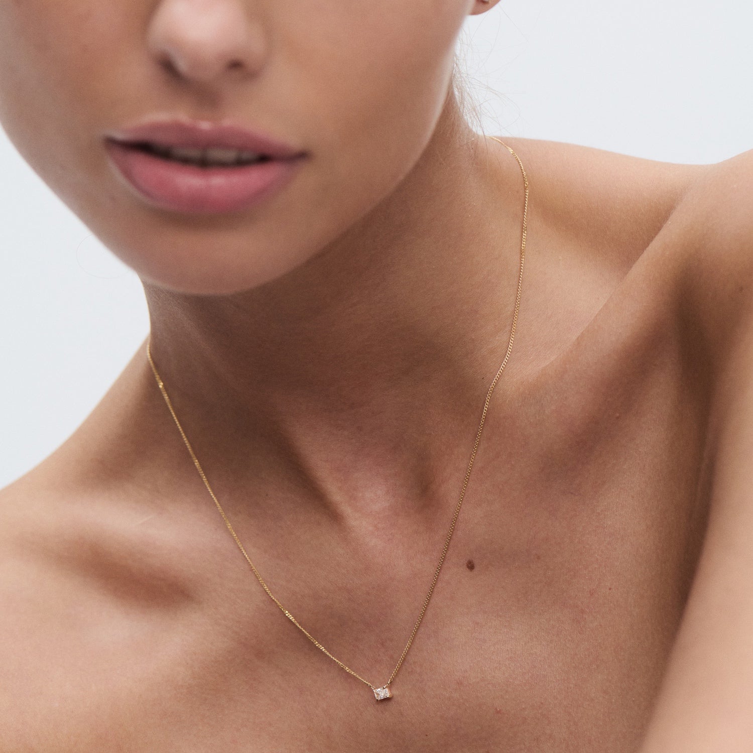 Close-up of a woman wearing an elegant gold necklace with a small diamond pendant. Ideal for luxury jewellery and fashion enthusiasts.
