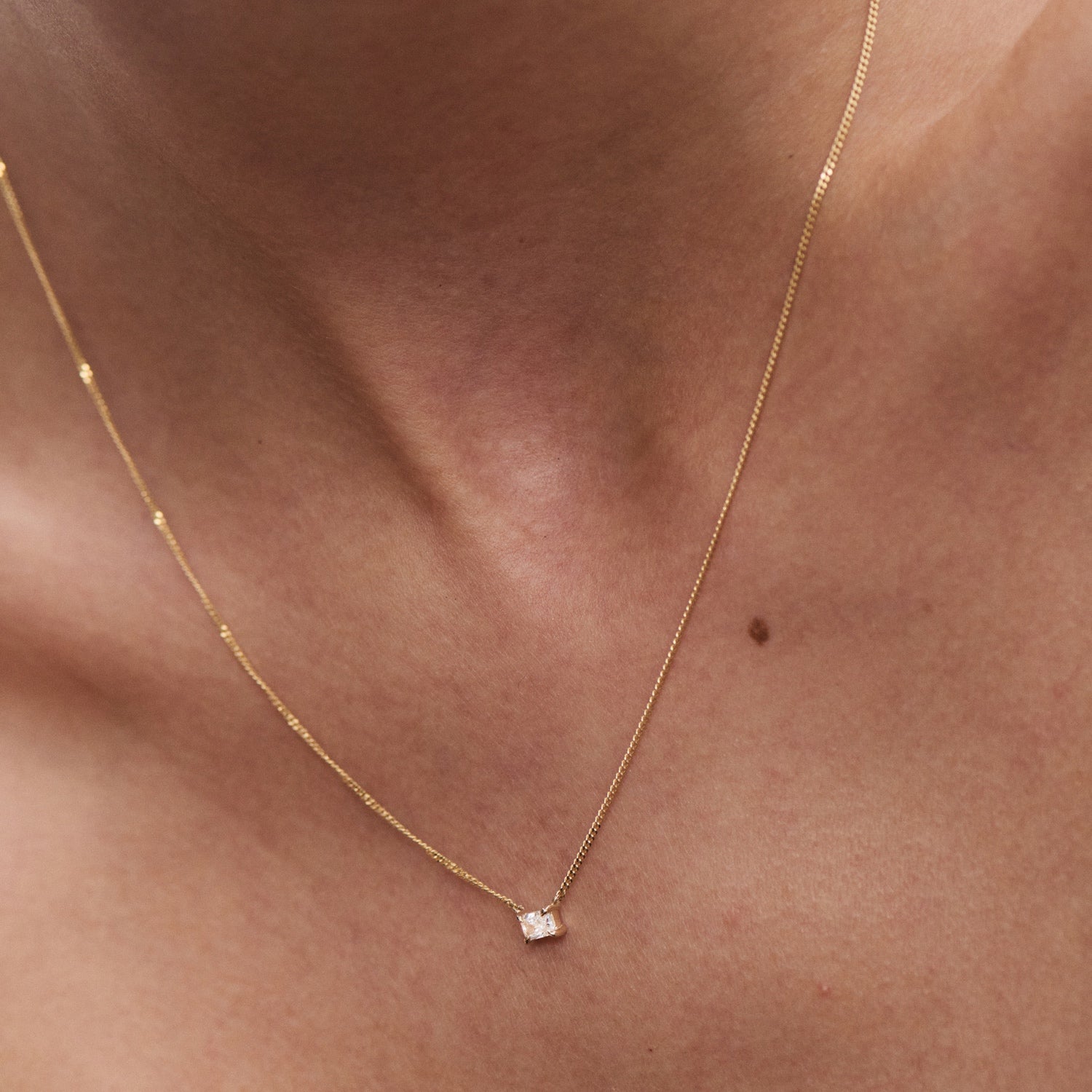 Close-up of a delicate gold necklace with a small, sparkling diamond pendant on a person's neck, symbolising luxury and elegance.