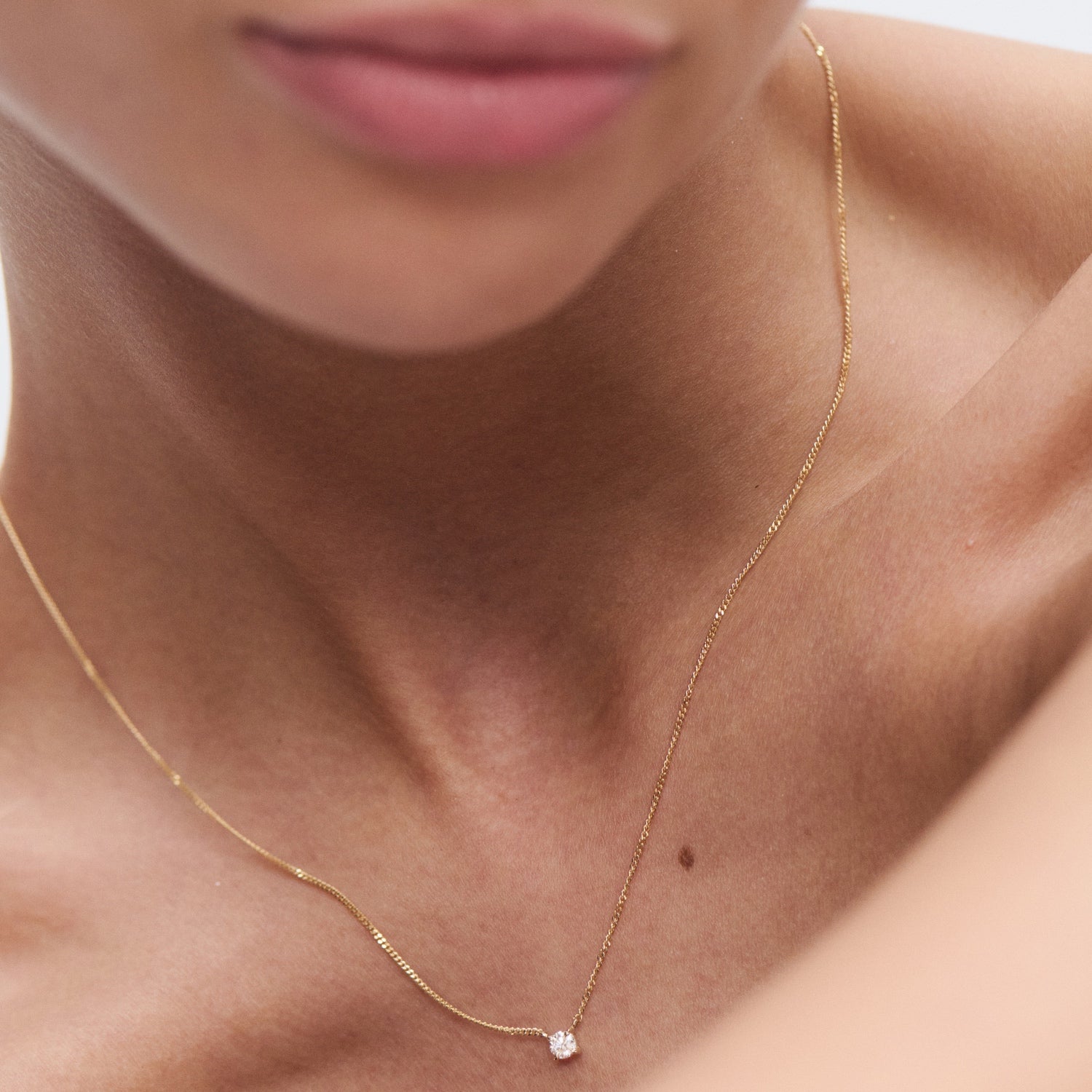 Close-up of a delicate gold necklace with a single diamond pendant, worn by a person with smooth skin. Minimalist luxury jewellery.