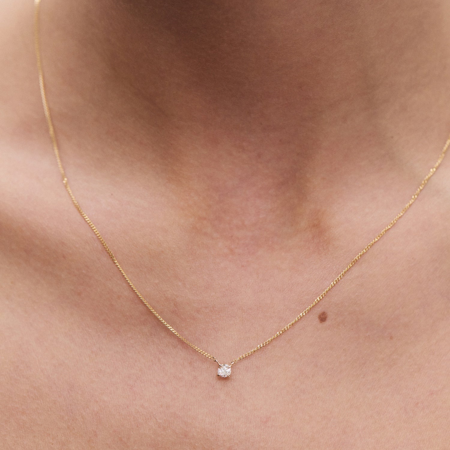 Delicate gold chain necklace with a single diamond pendant, elegantly resting on a woman's neck, symbolising luxury and sophistication.