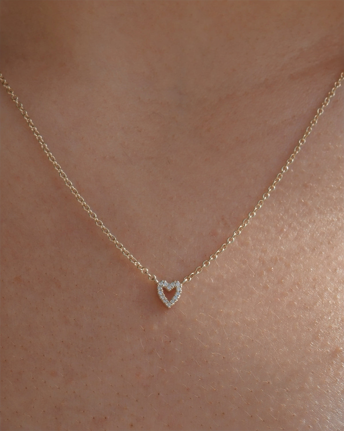 A delicate gold chain necklace with a small heart-shaped pendant set with tiny lab grown diamonds, shown worn on a person's neck.