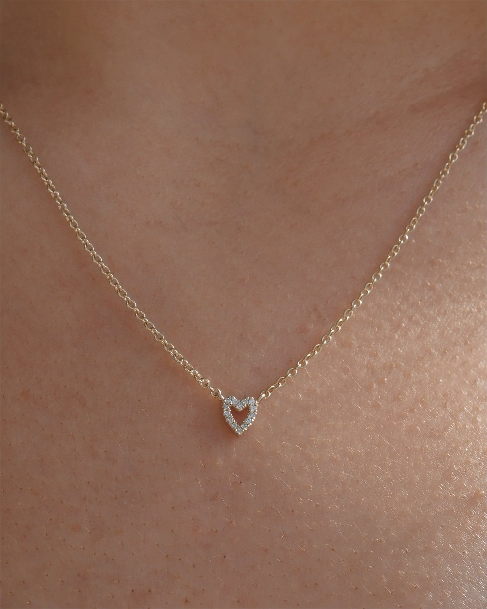 A delicate gold chain necklace with a small heart-shaped pendant set with tiny lab grown diamonds, shown worn on a person's neck.