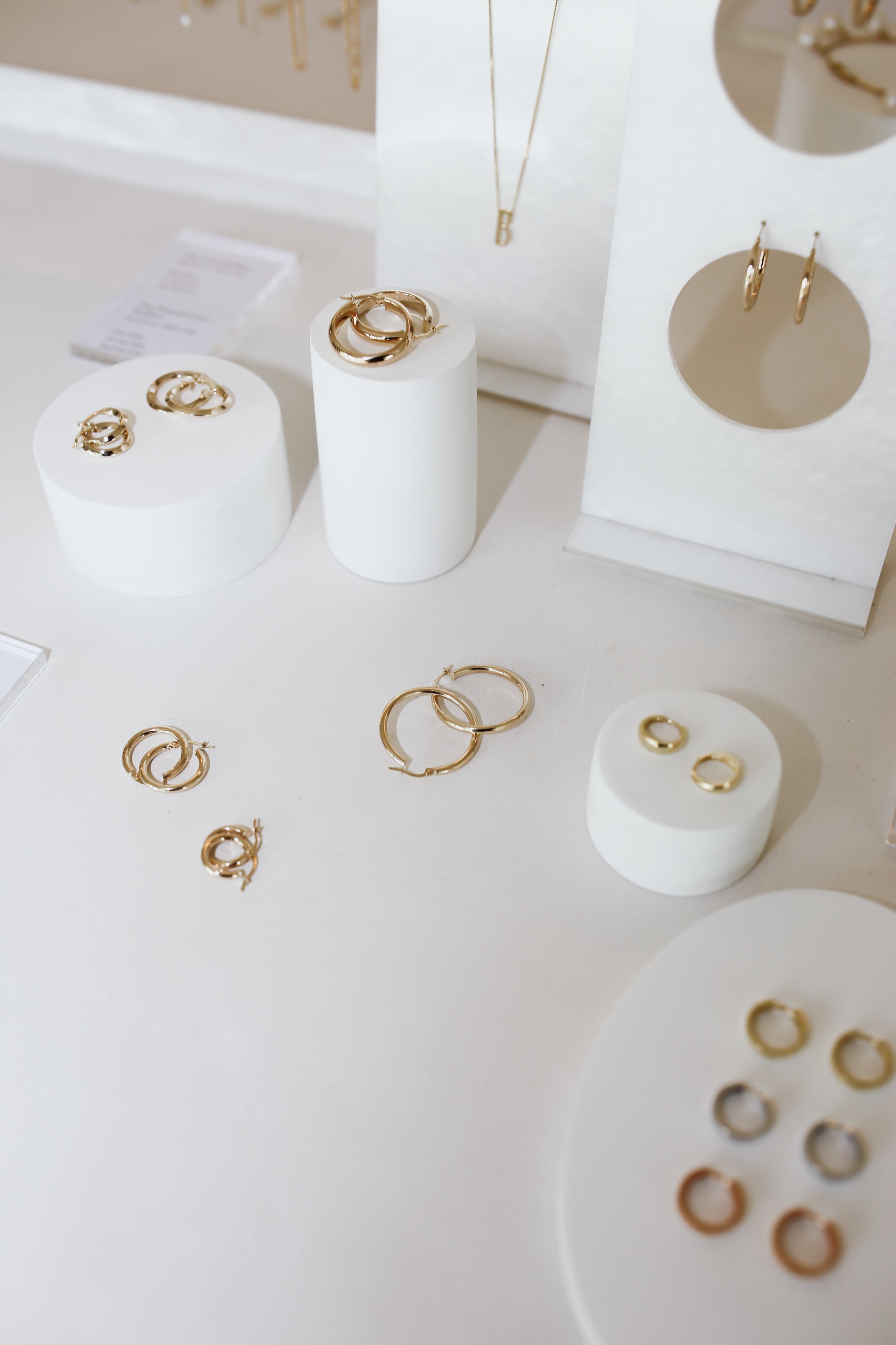 Assorted gold jewellery including rings, earrings, and necklaces displayed elegantly on white stands in a luxury showroom setting.