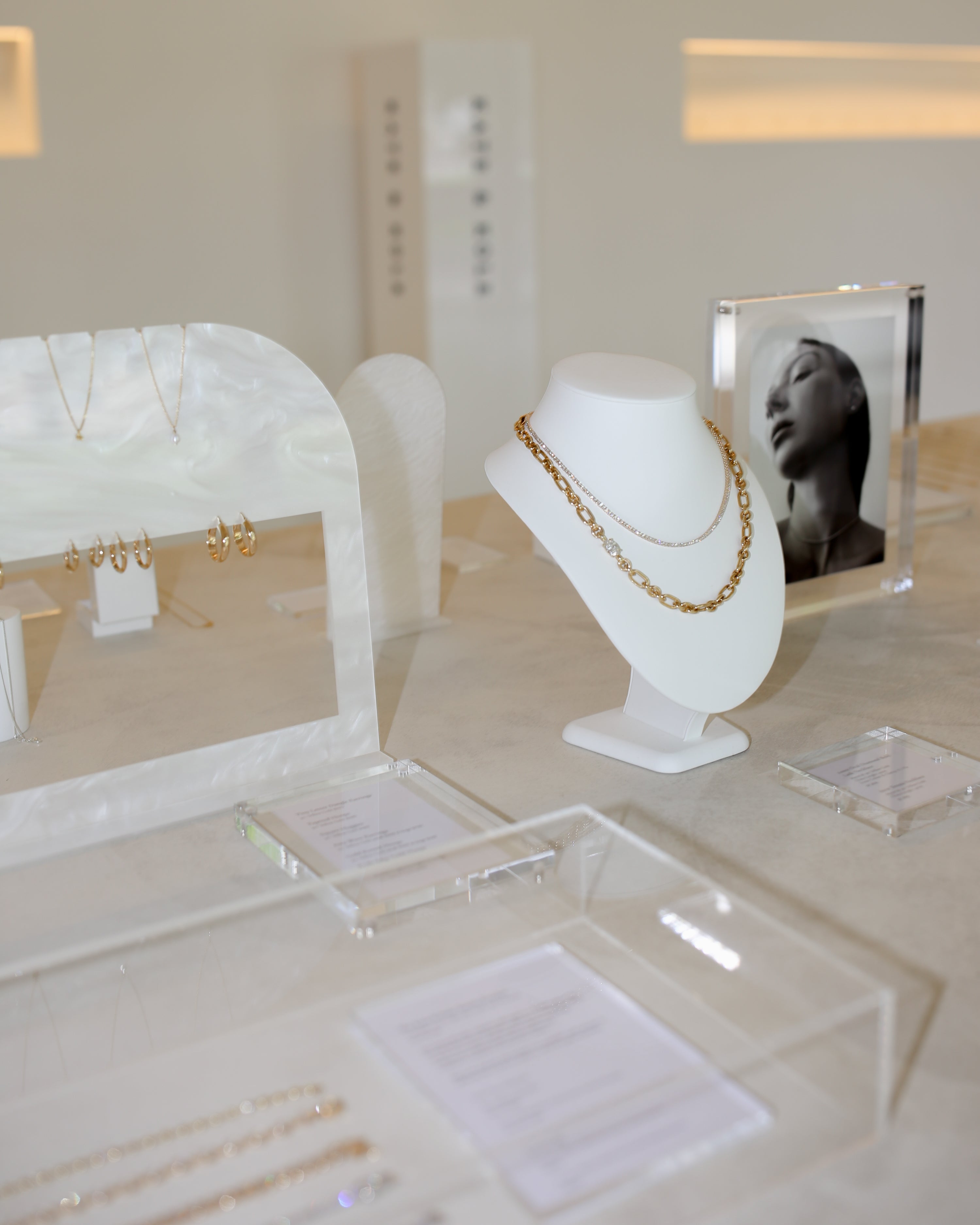 Display of luxury gold jewellery on white stands, featuring necklaces and earrings, with elegant promotional visuals in the background.