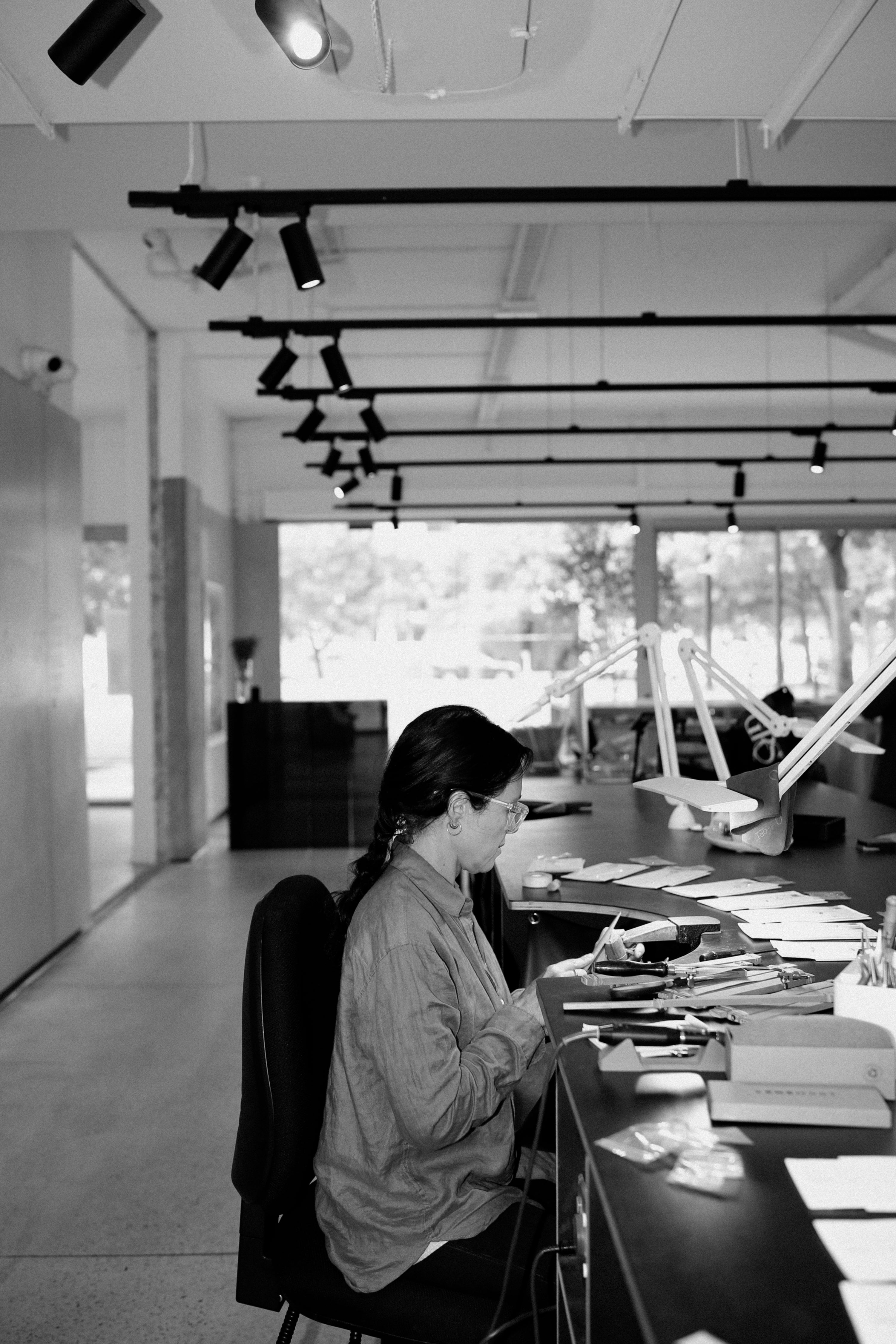 Jewellery artisan meticulously works at a modern, well-lit studio bench. Spotlights and organised tools create an elegant, luxurious atmosphere.
