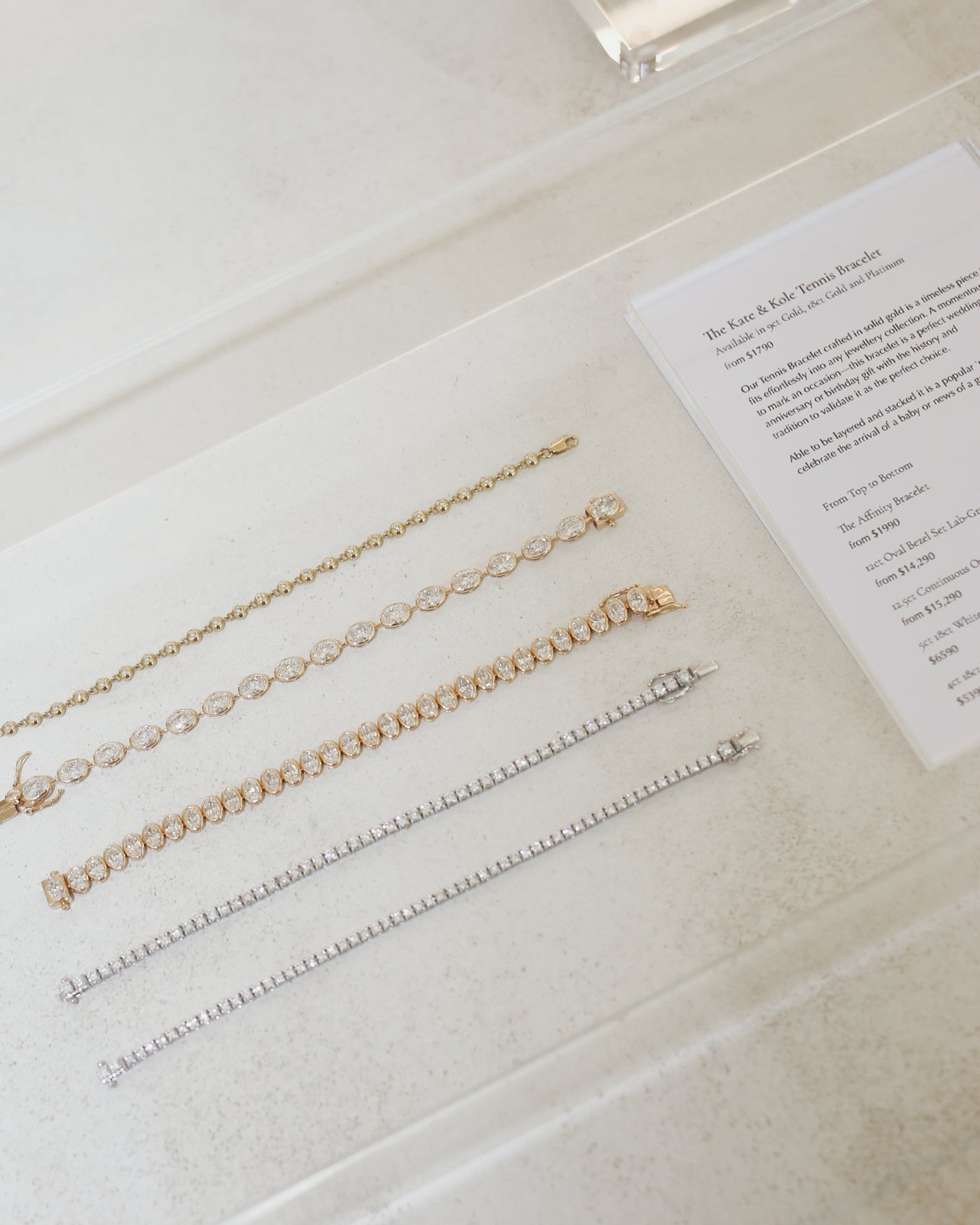 Display of five luxury tennis bracelets in gold and silver on a white surface, accompanied by a descriptive card.