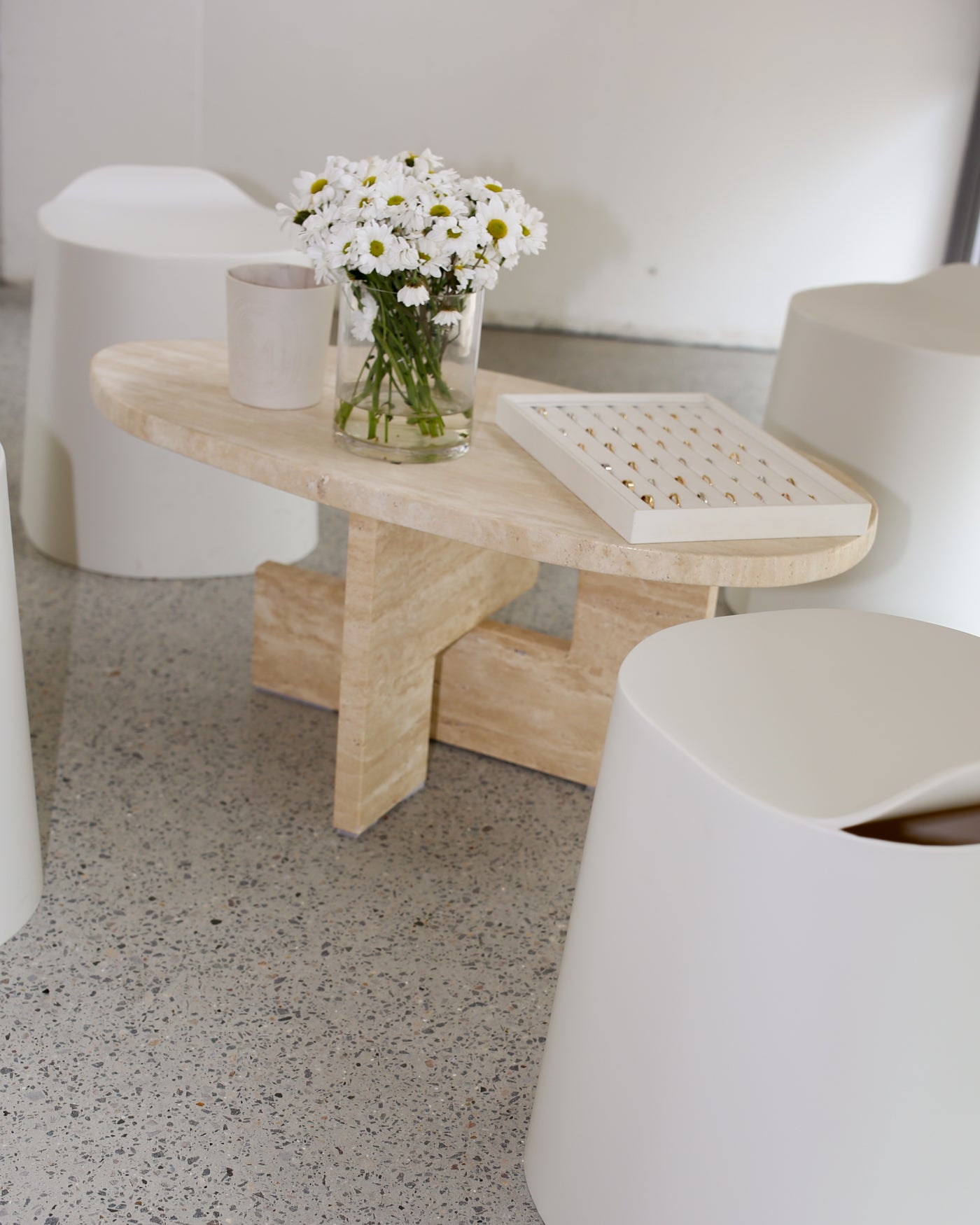 Minimalist setting with a wooden coffee table featuring daisies in a glass vase and a jewellery box. Surrounded by white, modern seating.