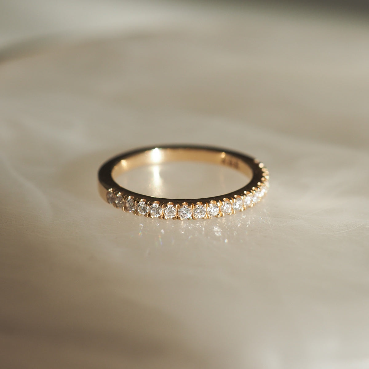Gold ring with sparkling diamonds set around the band, elegantly displayed on a soft, light-filled surface, showcasing luxury jewellery design.