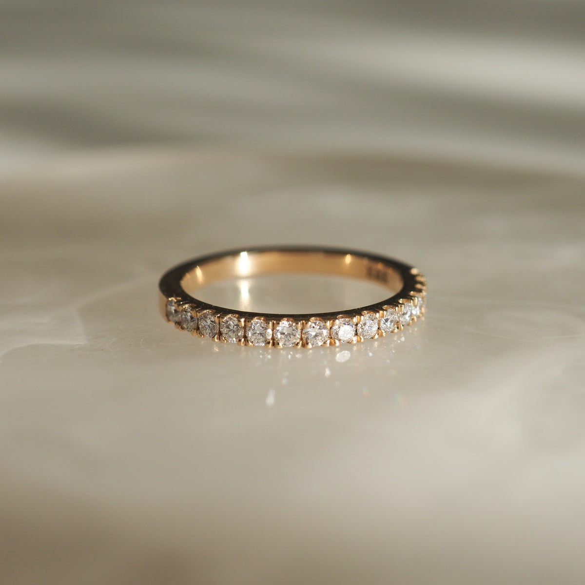 Gold band with round-cut diamonds halfway set, reflecting light on a smooth marble surface. Elegant and minimal luxury jewellery piece.