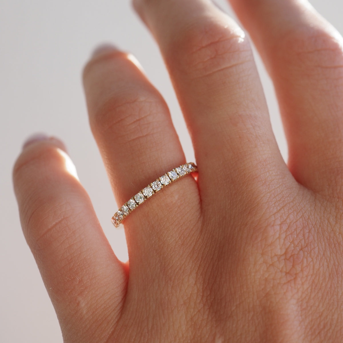 Gold eternity band featuring a row of sparkling diamonds, worn on a woman's hand. Luxury jewellery with elegant, minimalist design.