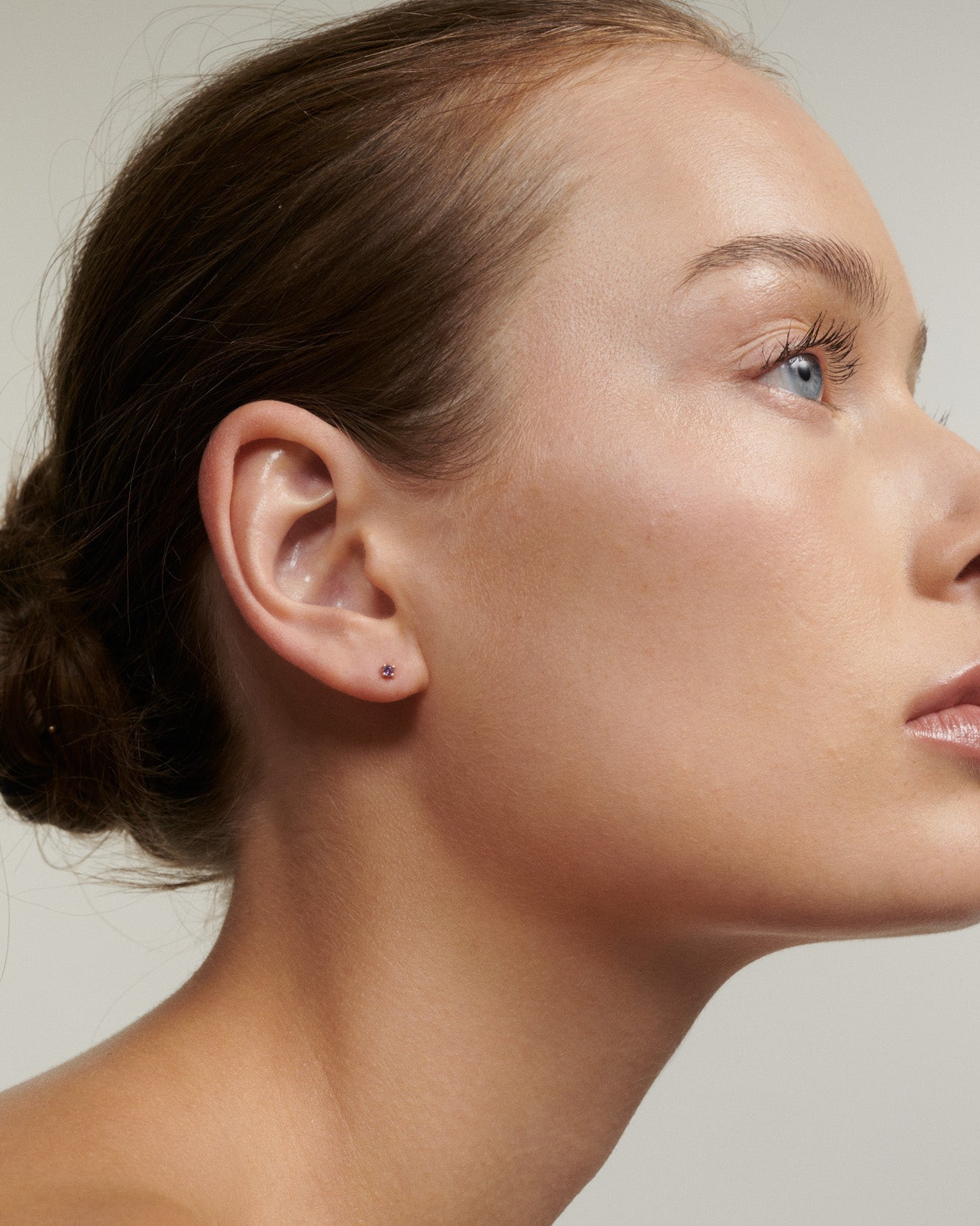 Close-up of a woman's ear with a small earring against a neutral background