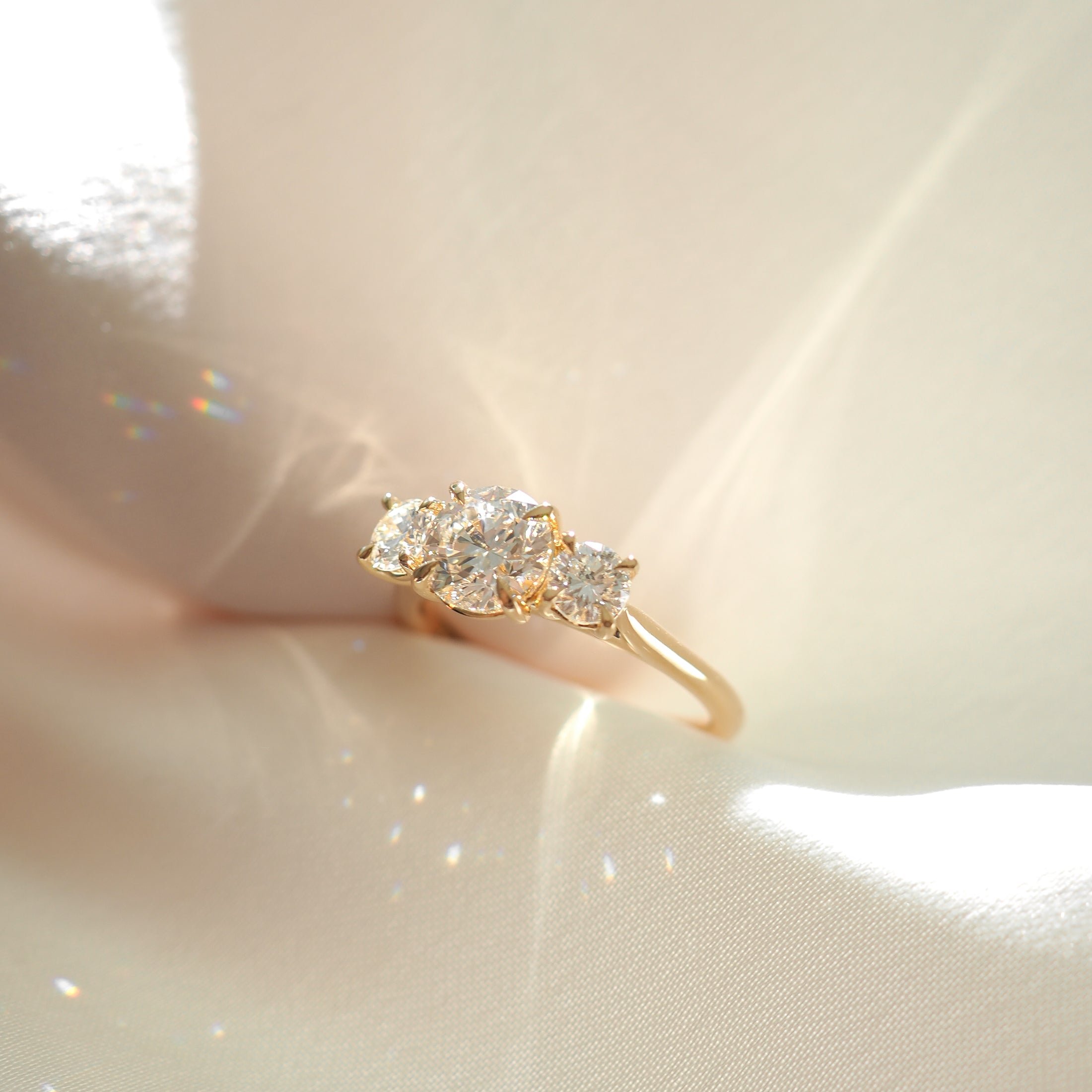 Elegant gold ring with three sparkling diamonds, displayed on soft satin fabric with subtle light reflections. Perfect for luxury jewellery lovers.