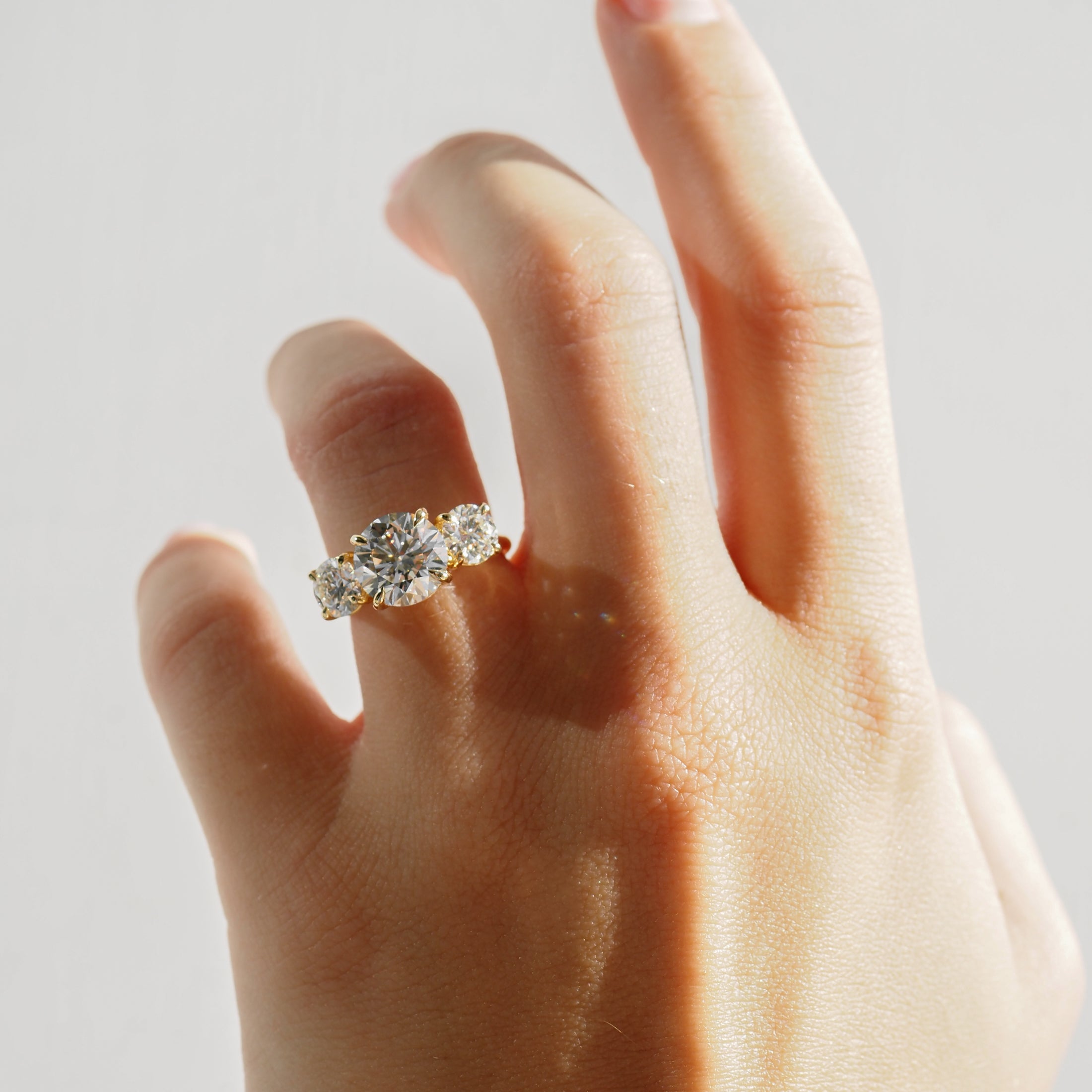 Hand wearing a luxurious three-stone diamond ring against a soft light background, showcasing high-end jewellery details and craftsmanship.