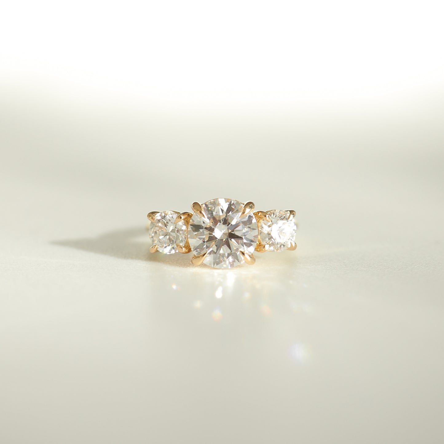 Luxury gold ring with three round diamonds, sparkling in soft light, on a pale background. High-end jewellery elegance.
