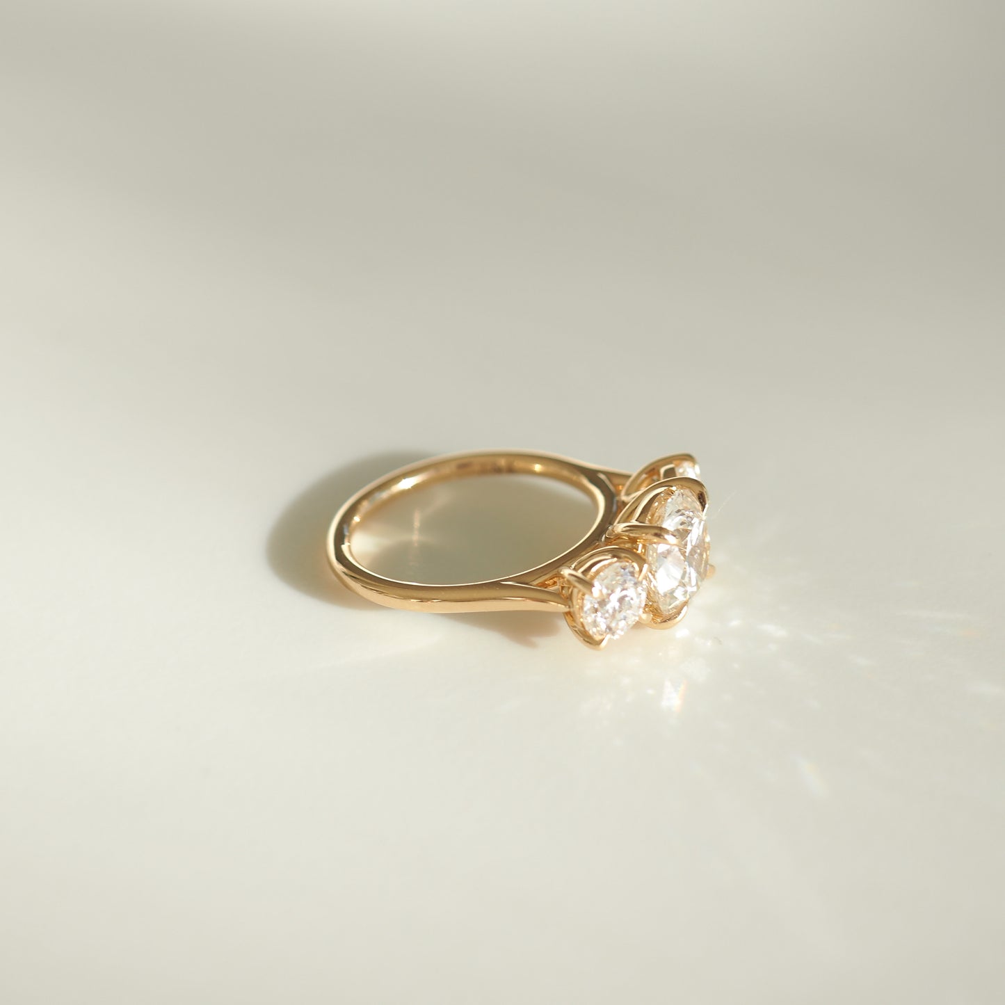 Gold ring with three sparkling diamonds set side by side, reflecting light on a soft beige background. Perfect luxury jewellery piece.