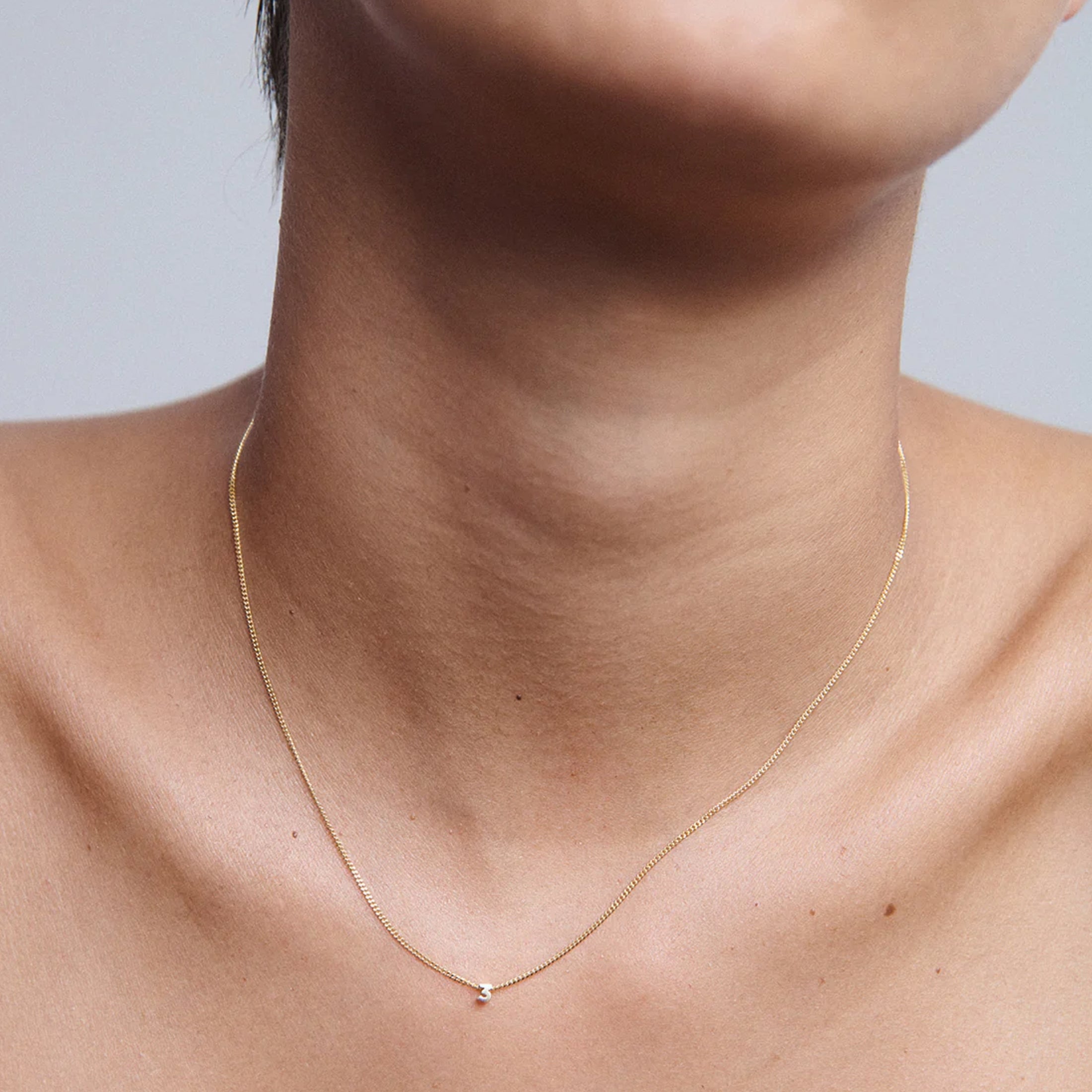 Close-up of a gold necklace with a small diamond pendant on a person's neck. Simple, elegant jewellery design; luxury and minimalist style.