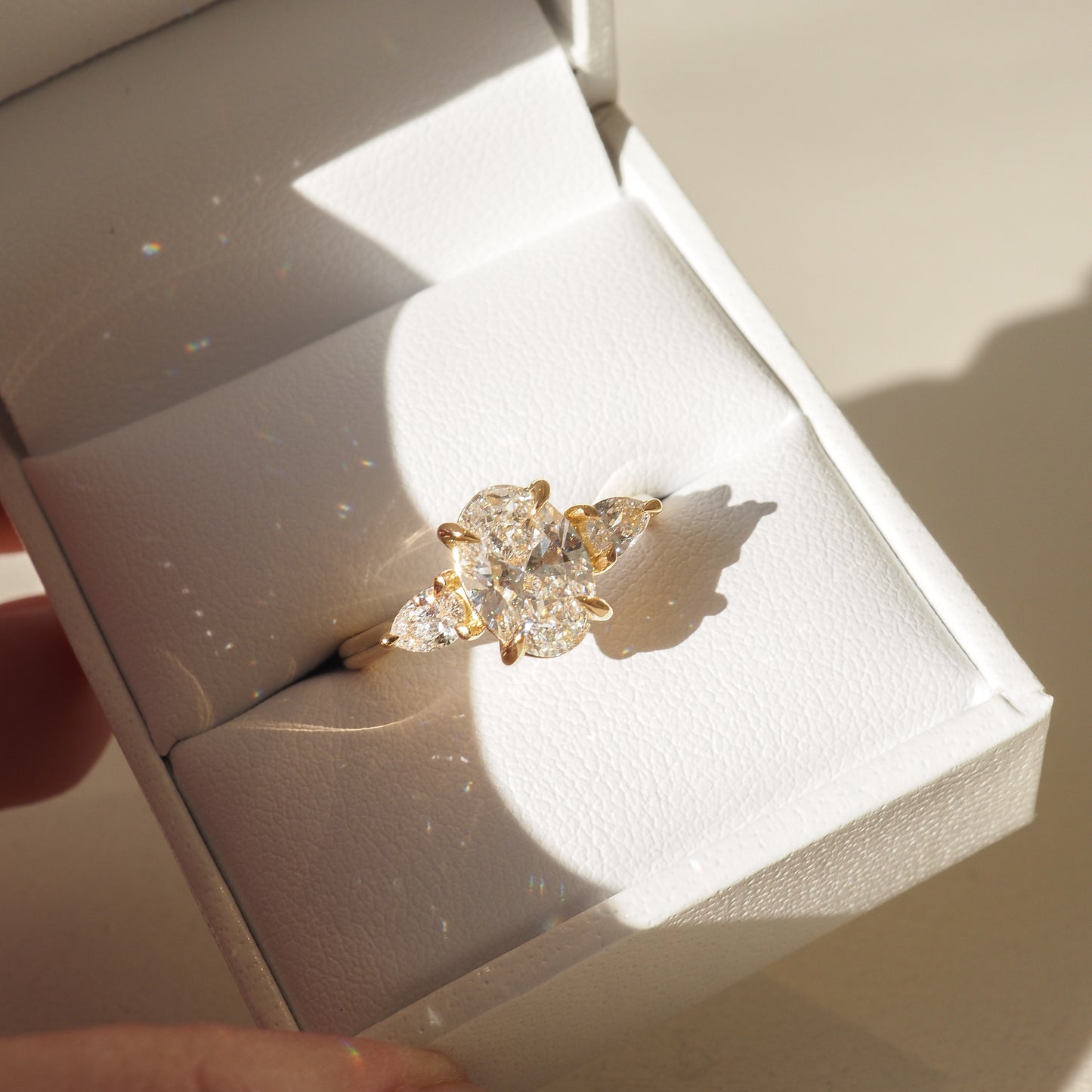 Elegant gold ring with a large marquise-cut diamond displayed in a white jewellery box, illuminated by natural light.
