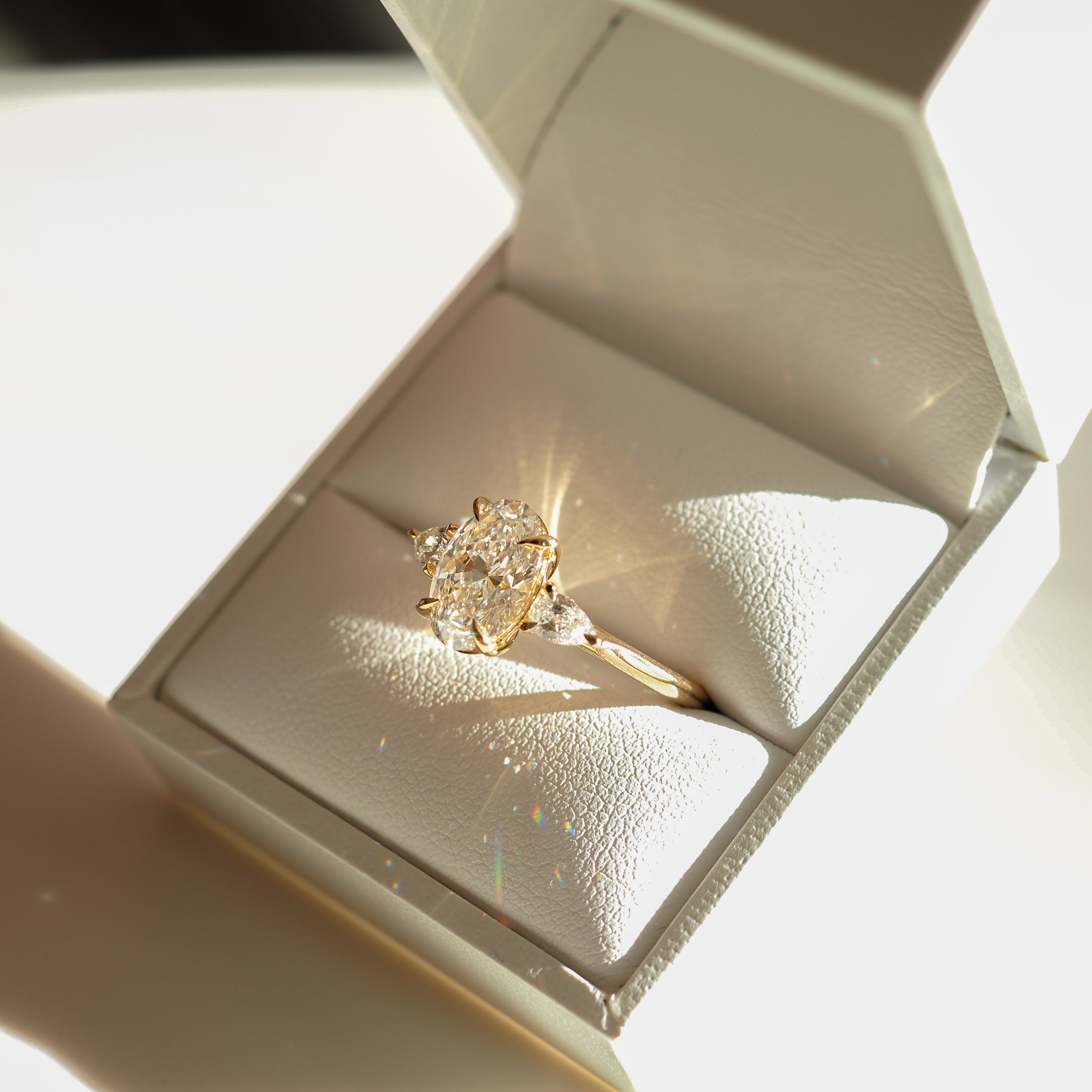 Elegant diamond ring with a large oval stone, set in a white jewellery box, sparkling under light. Luxurious and sophisticated design.