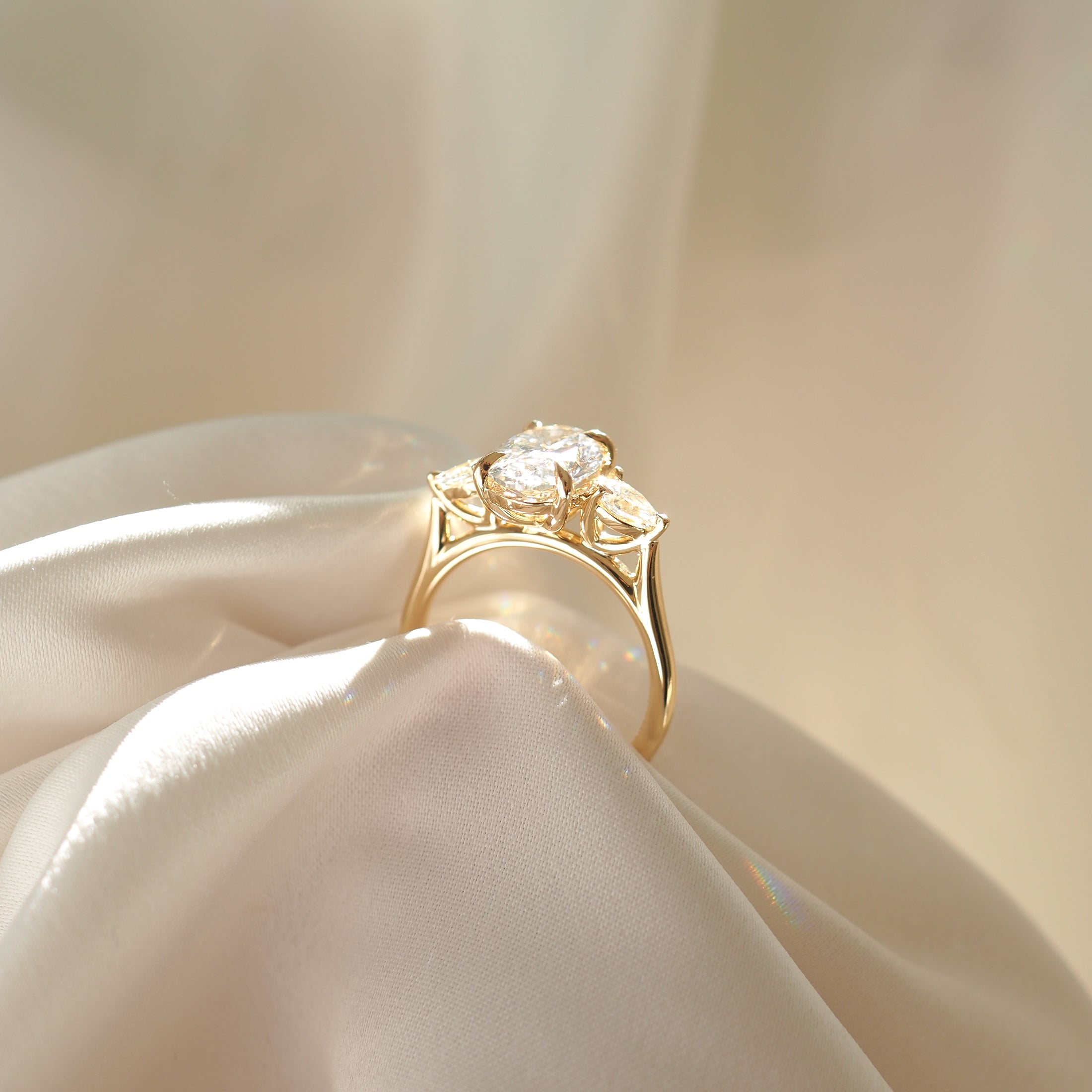Gold ring with three teardrop-shaped diamonds, elegantly displayed on soft, cream fabric, highlighting luxury jewellery design.