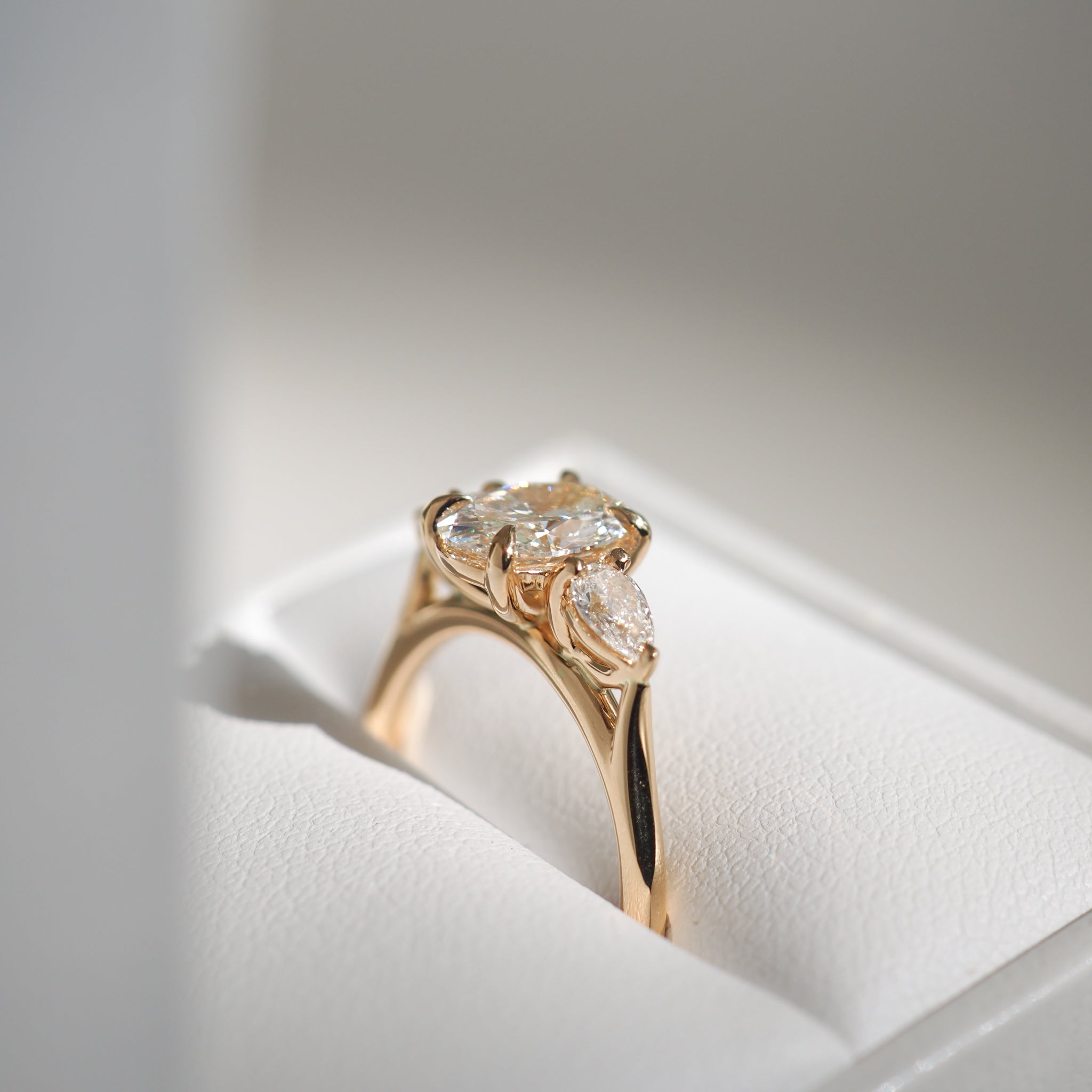 Gold ring with three oval diamonds set elegantly on a white cushion.