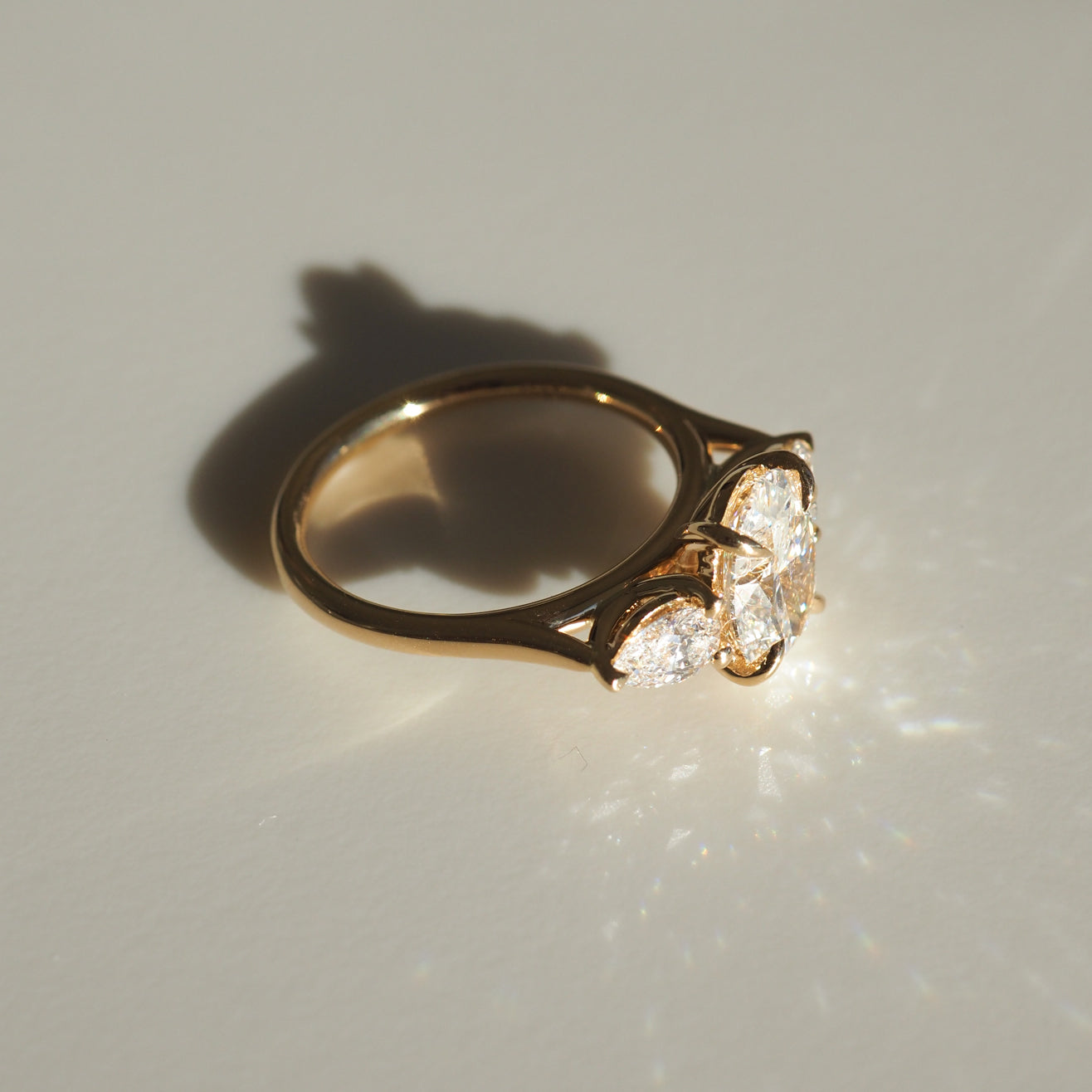 Gold ring with three large sparkling diamonds on a light surface, casting shadows. Luxurious jewellery piece, elegant and radiant design.