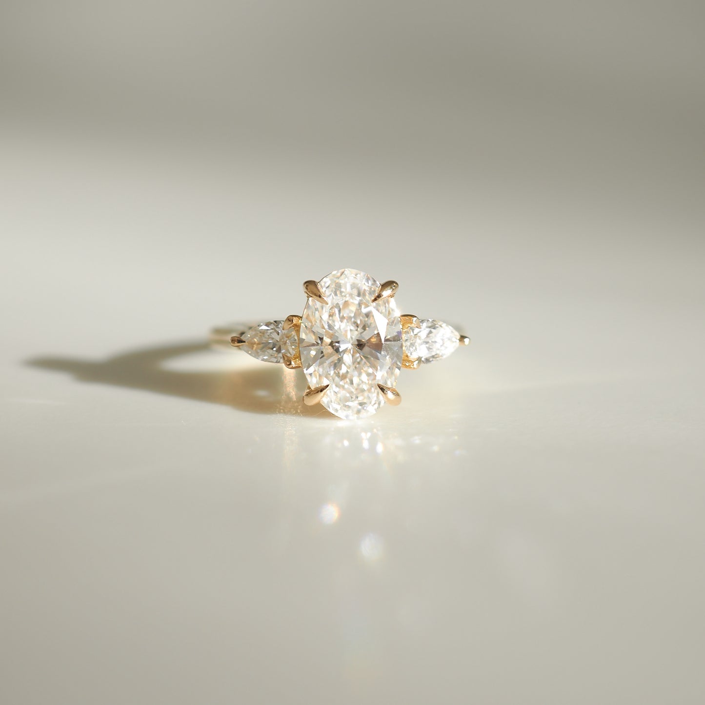 Gold ring with a large oval diamond centre, flanked by two smaller pear-shaped diamonds, on a glossy surface. Luxurious jewellery piece.