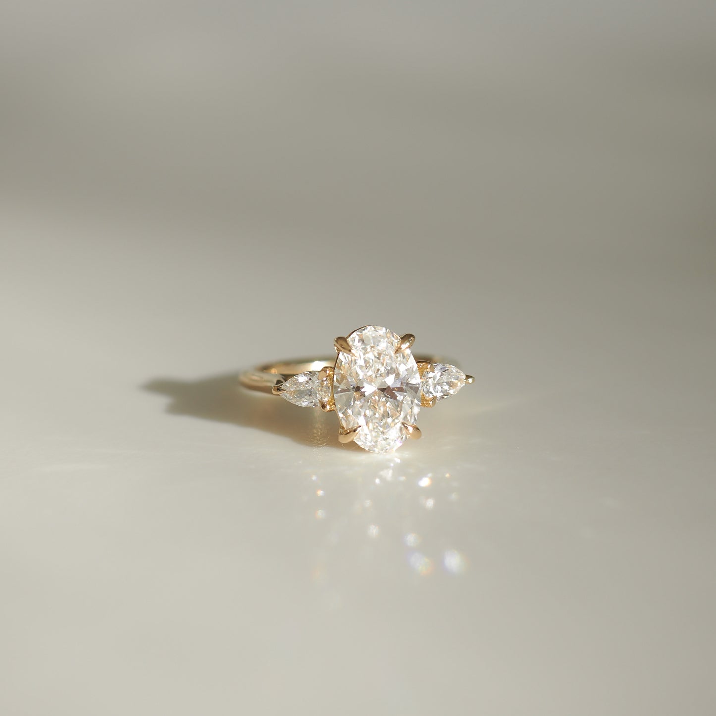 Elegant oval diamond ring with side stones set in gold, capturing light on a smooth surface. Luxurious high-end jewellery piece.