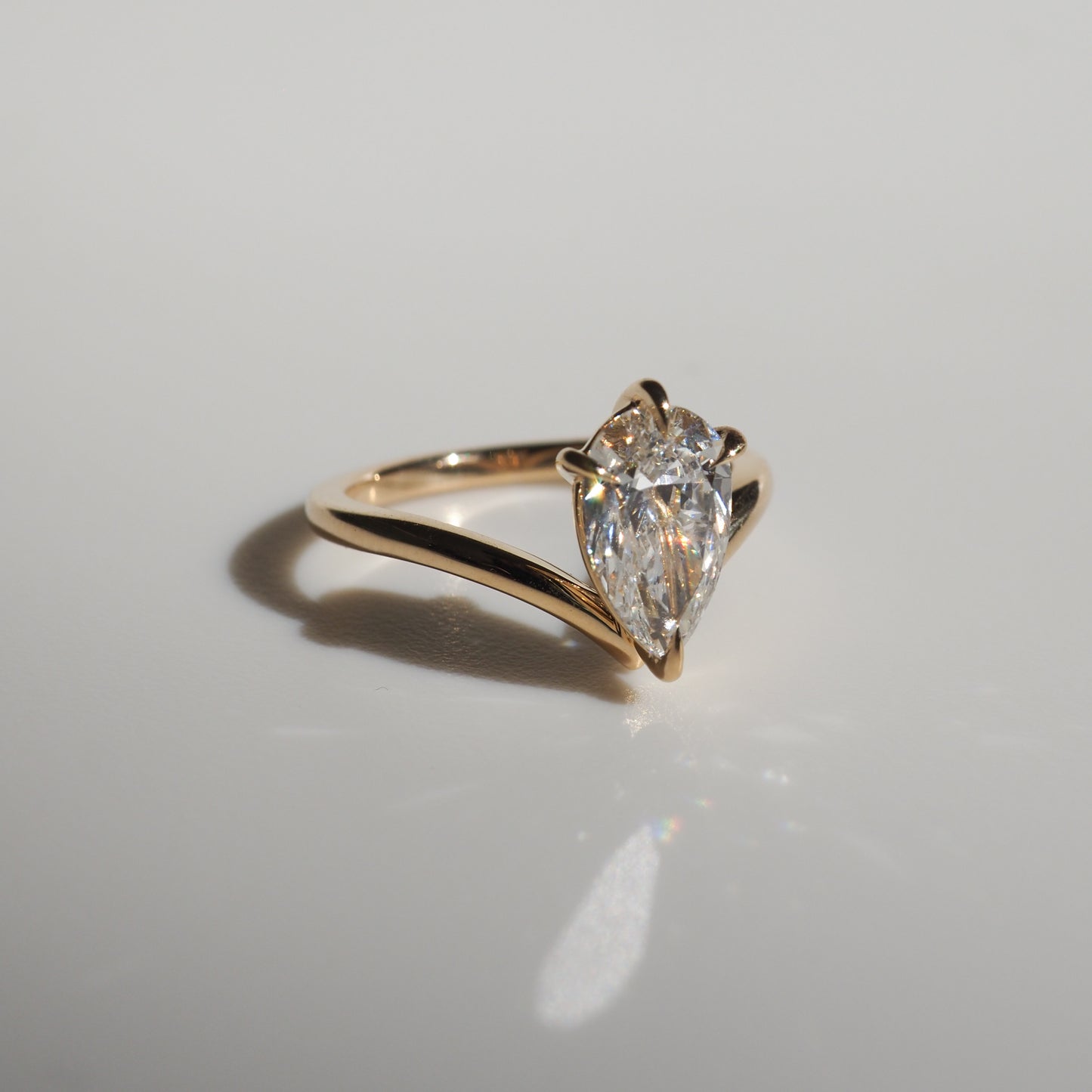 Gold ring featuring a pear-shaped diamond solitaire, elegantly set on a polished band, casting a soft shadow on a light surface.