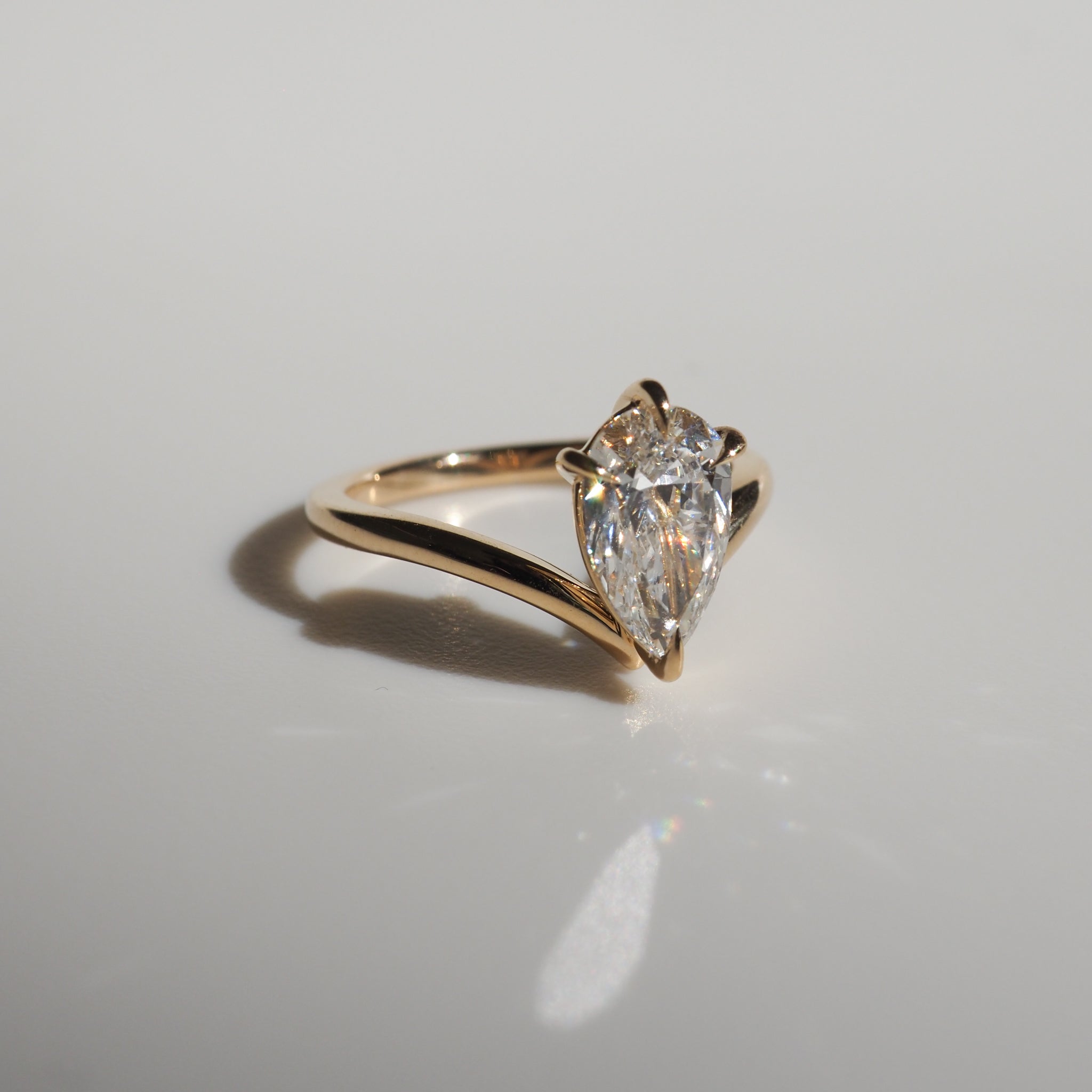 Gold ring featuring a pear-shaped diamond solitaire, elegantly set on a polished band, casting a soft shadow on a light surface.