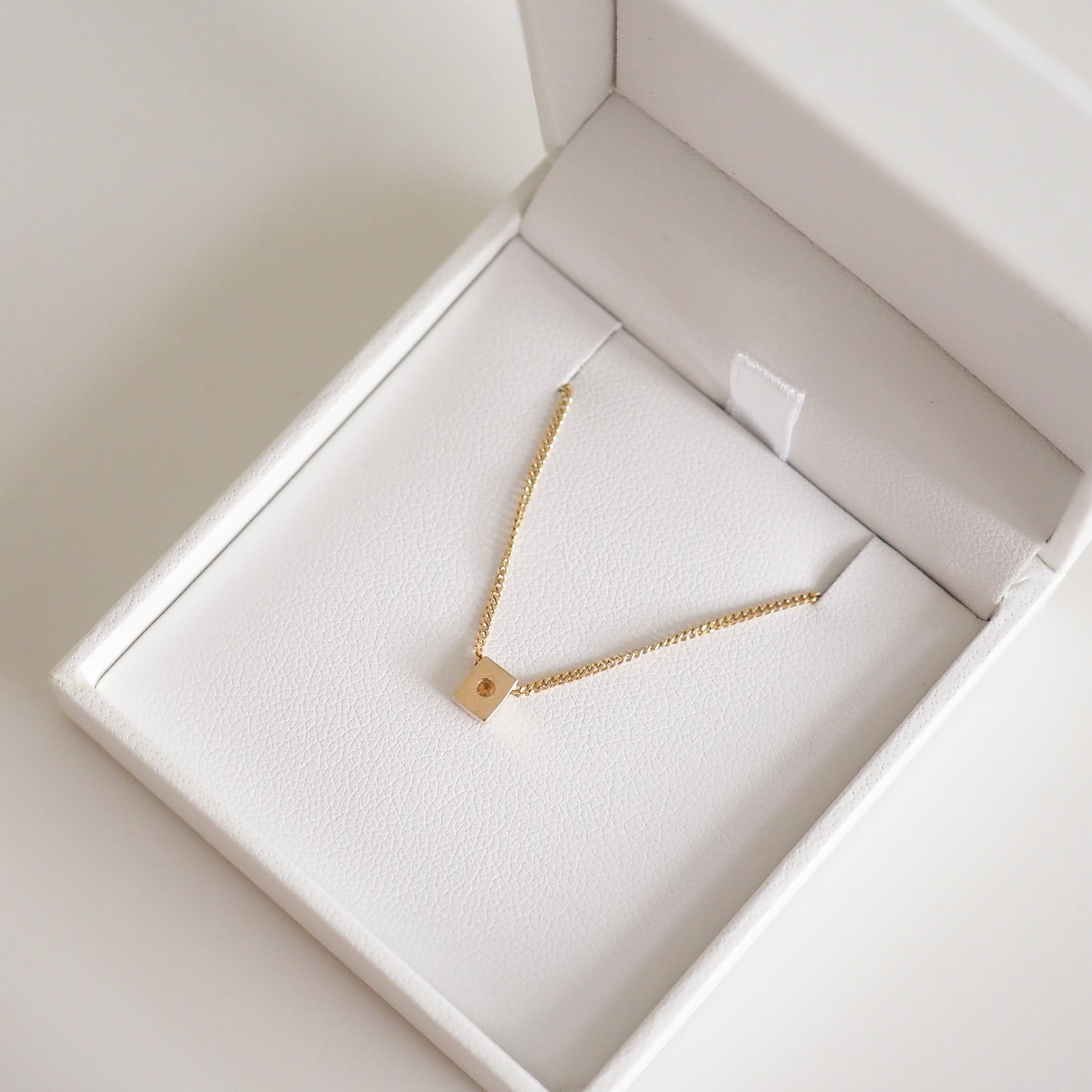 Gold chain necklace with a square pendant in a white jewellery box. Elegant design, luxury accessory, suitable for gifting.