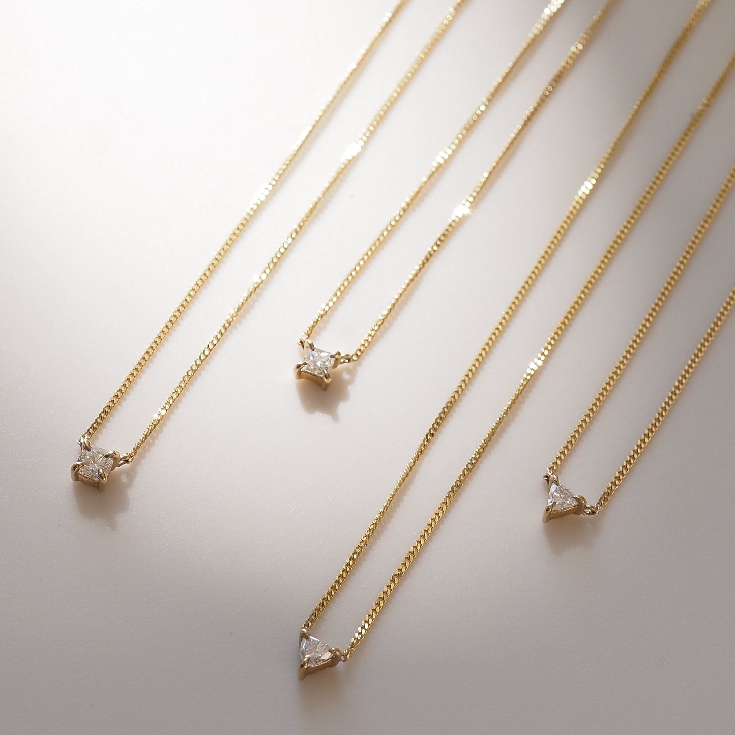 Four gold necklaces with diamond pendants on a light background