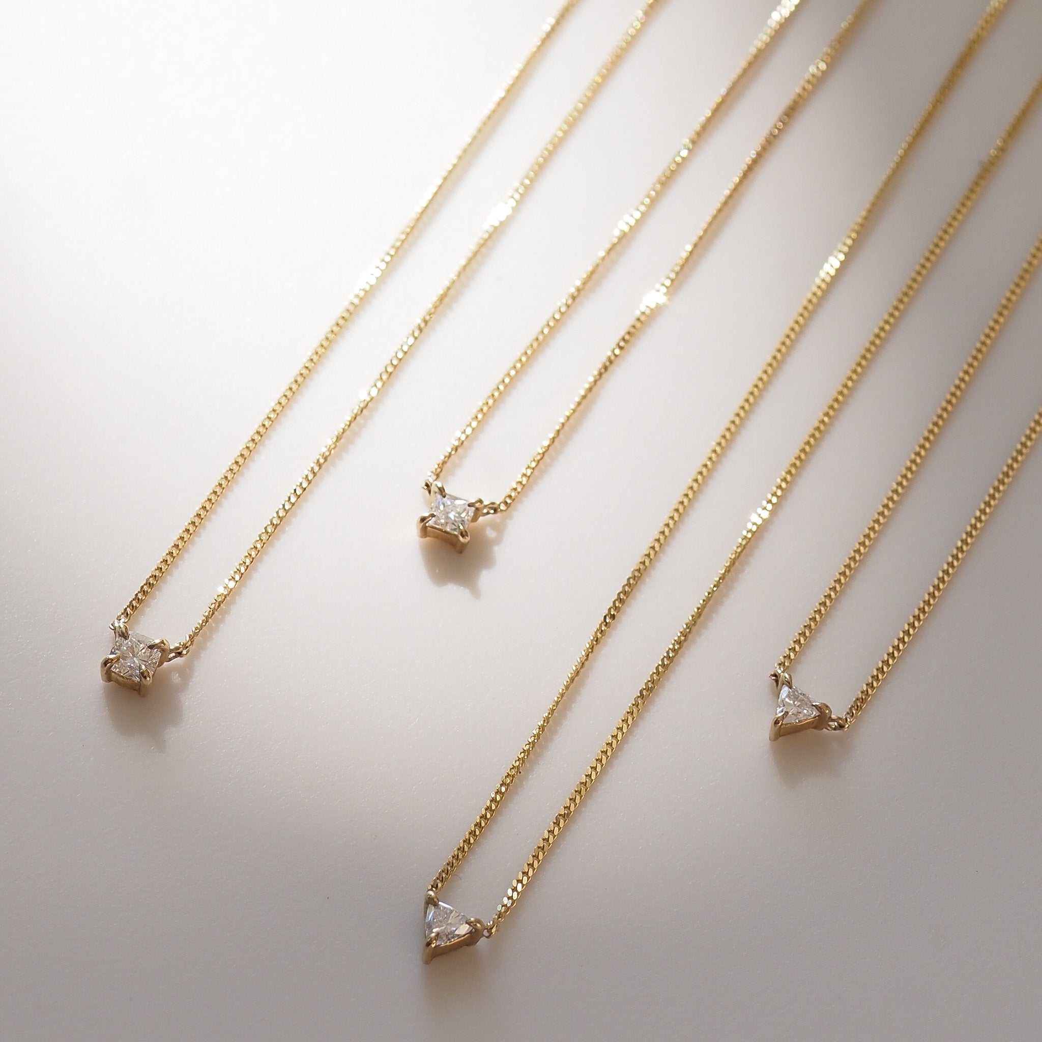 Four gold necklaces with diamond pendants on a light background